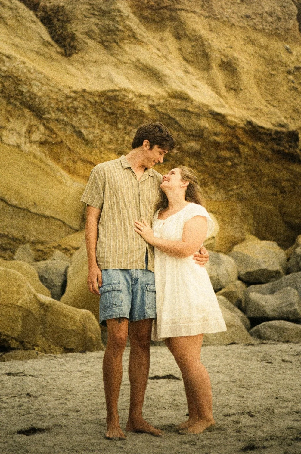Rose and Brady close together in front of a sandstone cliff at La Jolla Shores, shot on 35mm film