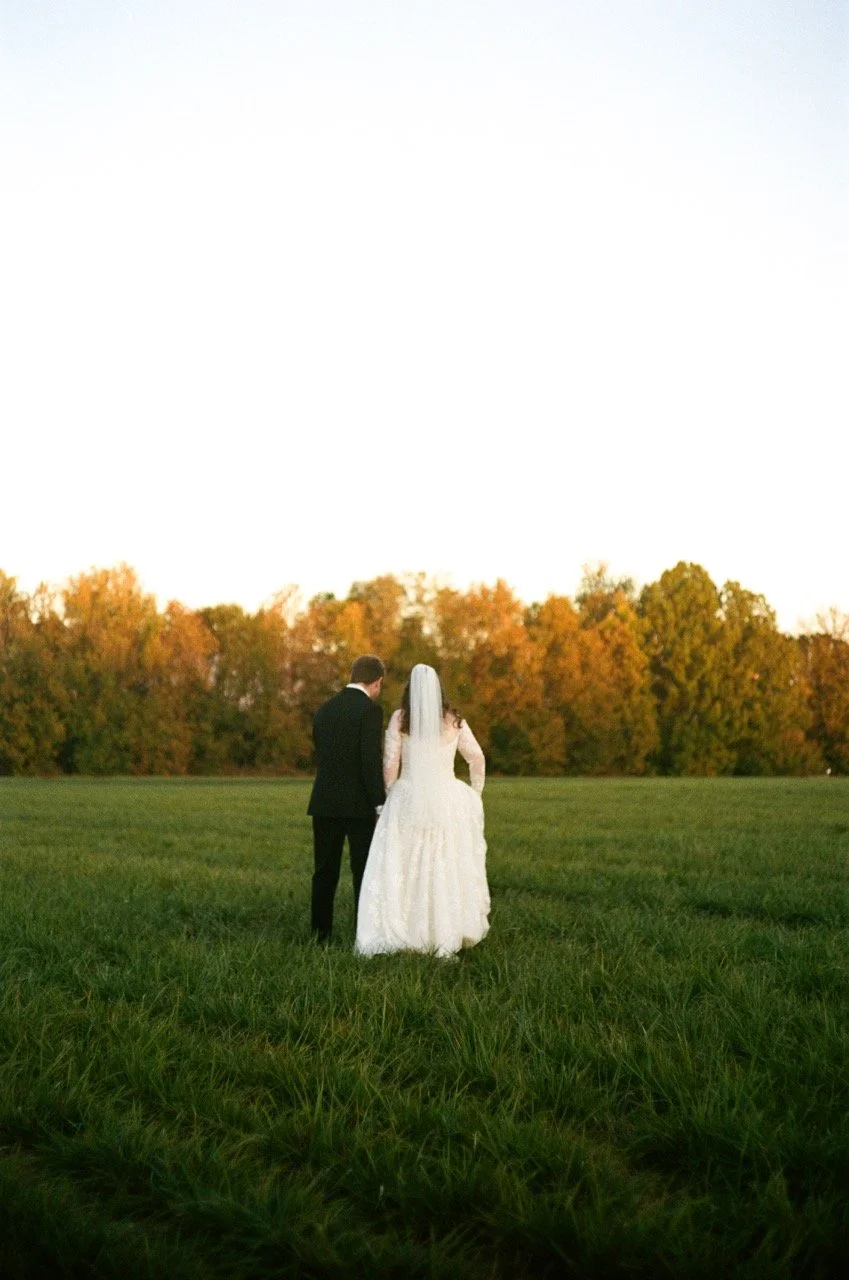 Carley and Preston standing together in the field in front of the trees, shot on film