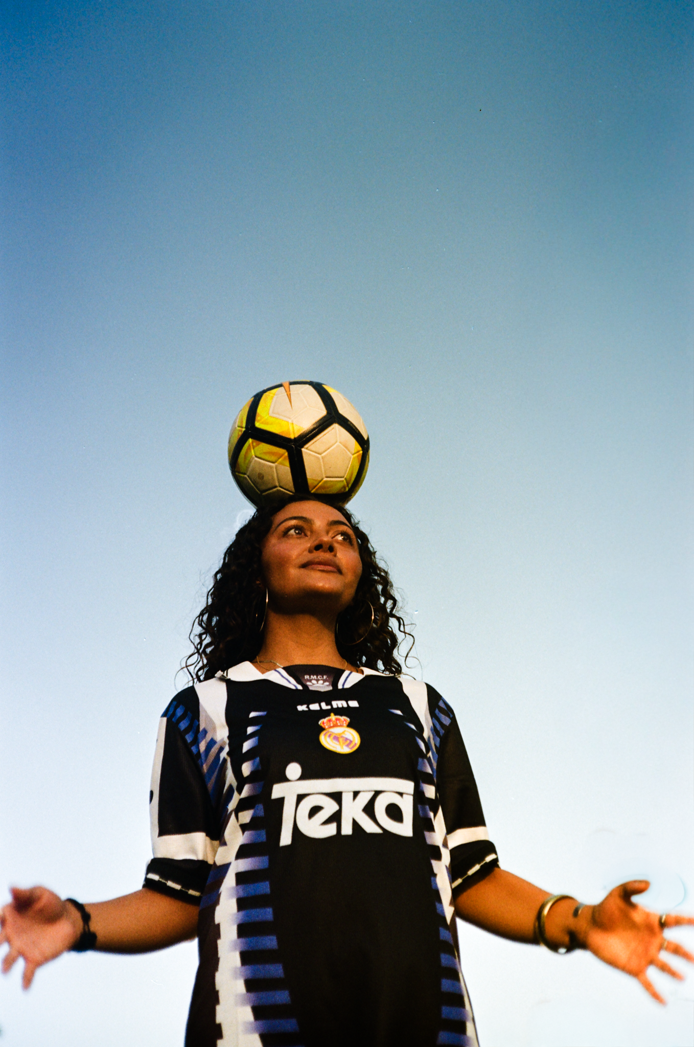 Jackie balancing a ball on her head in a vintage kit against a blue sky, shot on film