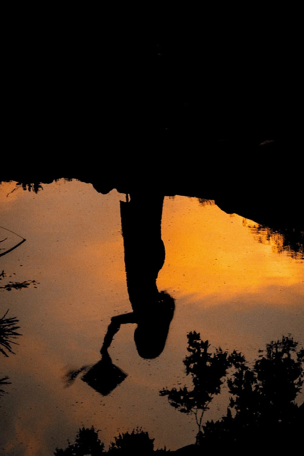Magaly’s reflection in the water, cap in hand at sunset