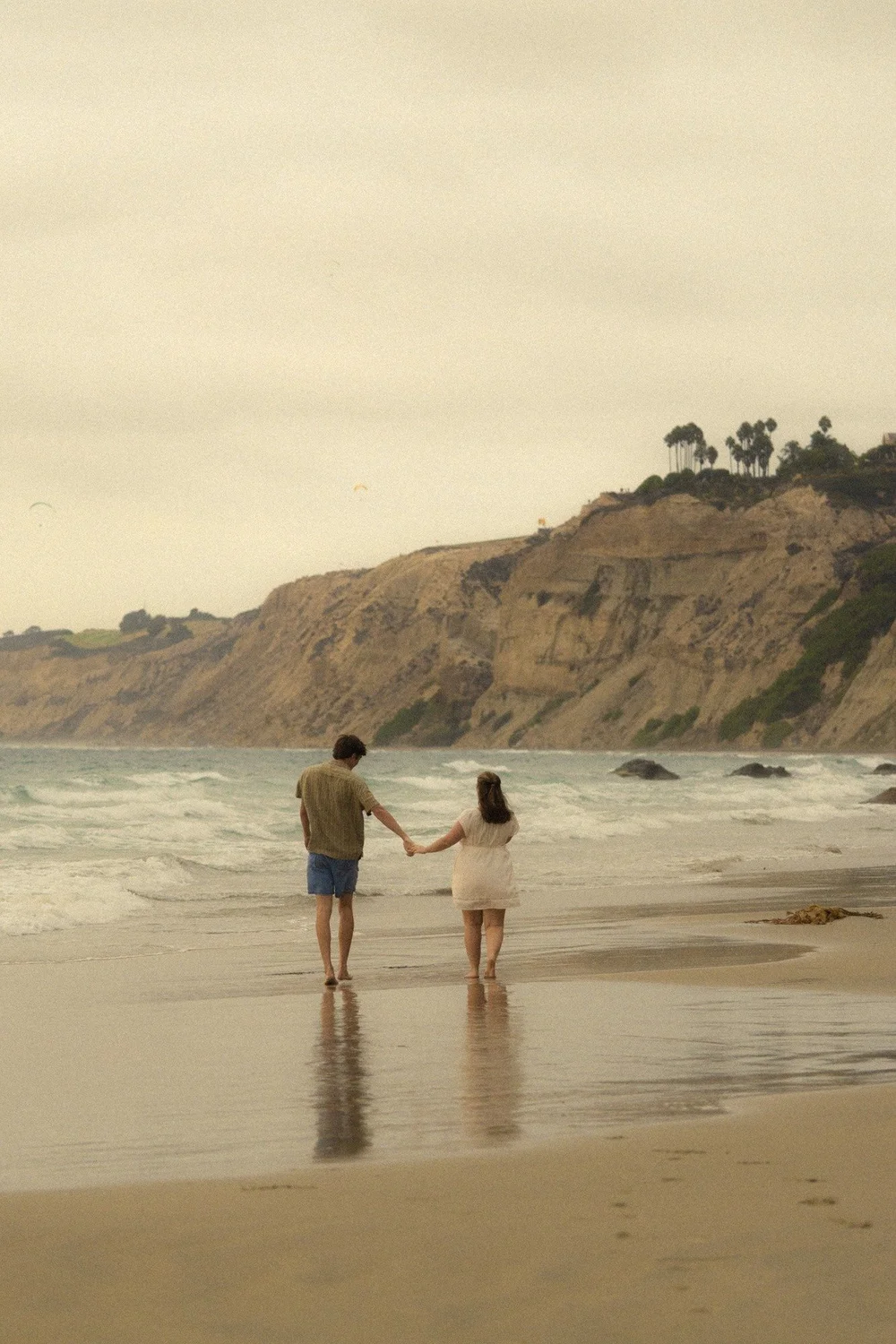 Rose and Brady walking hand in hand along the beach below the cliffs at La Jolla Shores