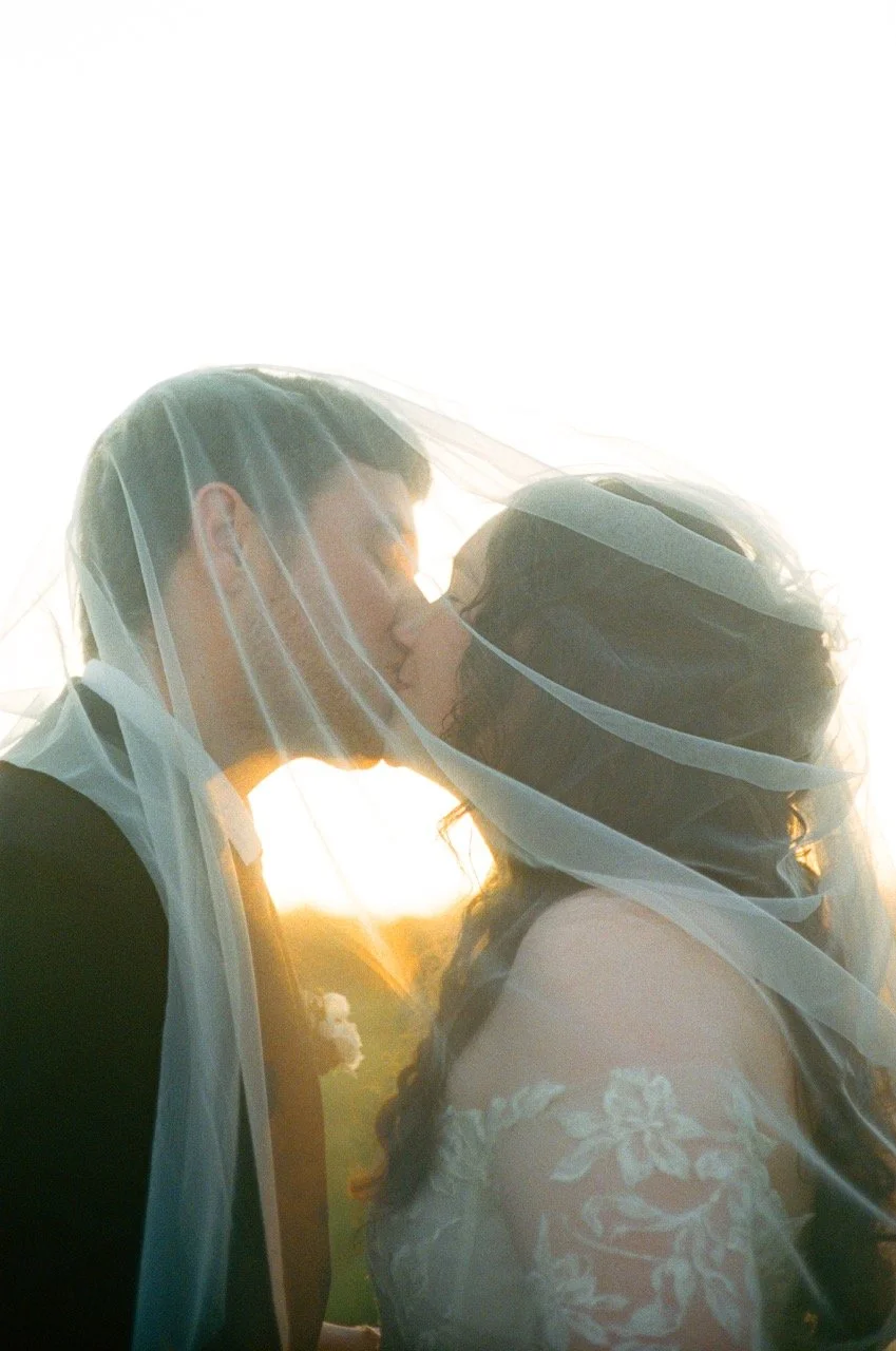 Carley and Preston kissing under her veil with the sun behind them, shot on film