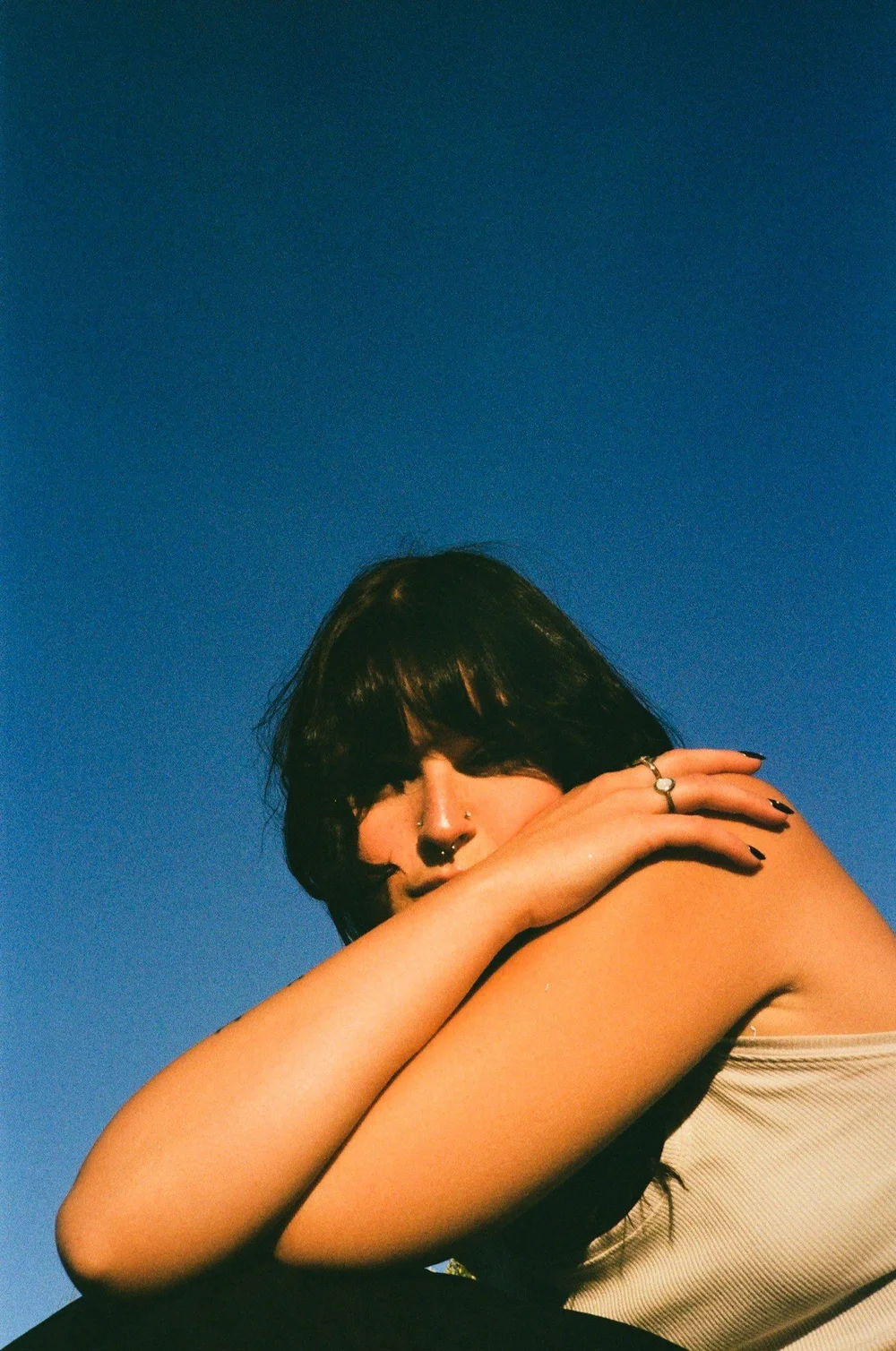 Laurel resting her face on her arms against a blue sky in El Cajon, shot on 35mm film