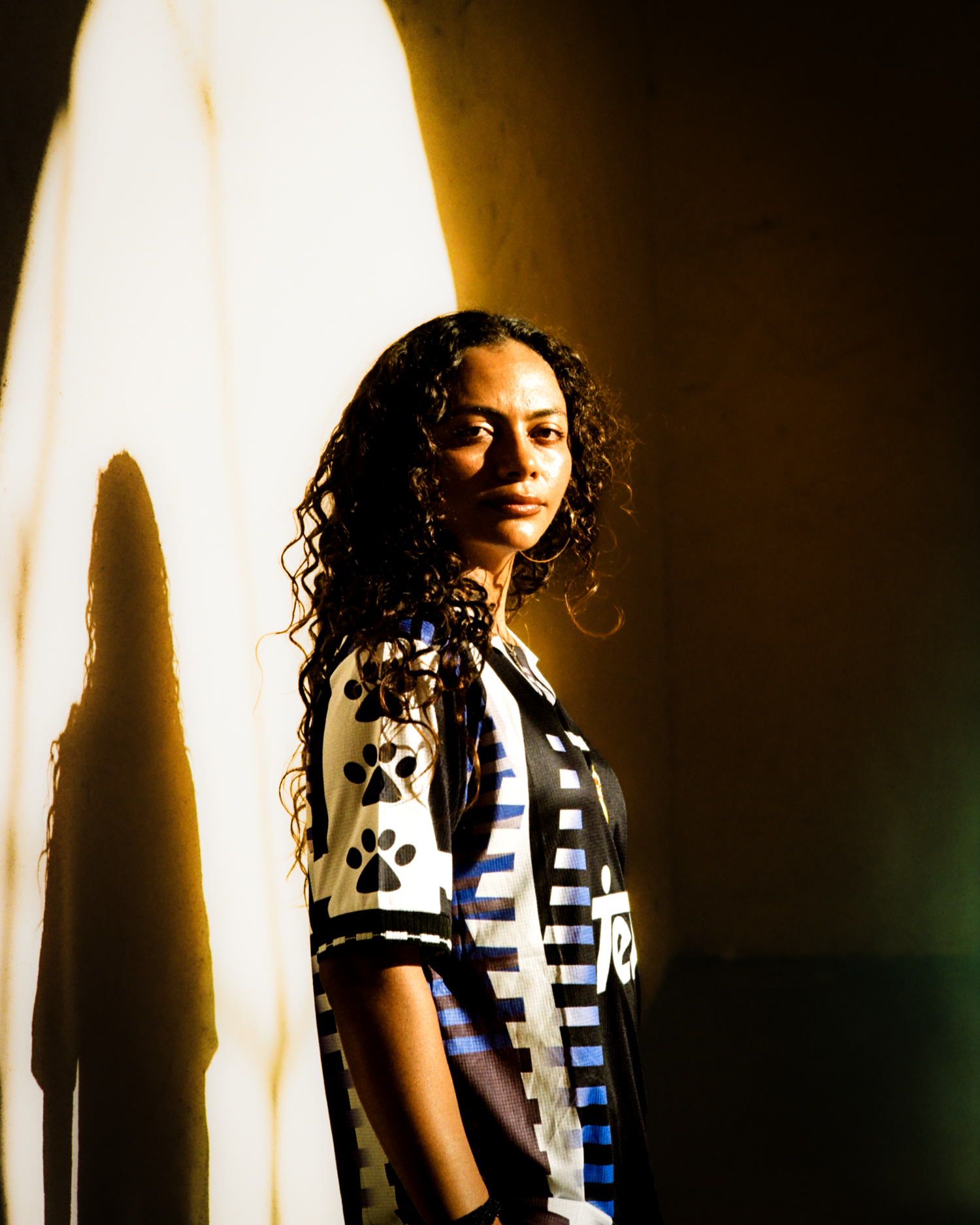 Jackie in a vintage kit against a warm wall with her shadow beside her, shot on film