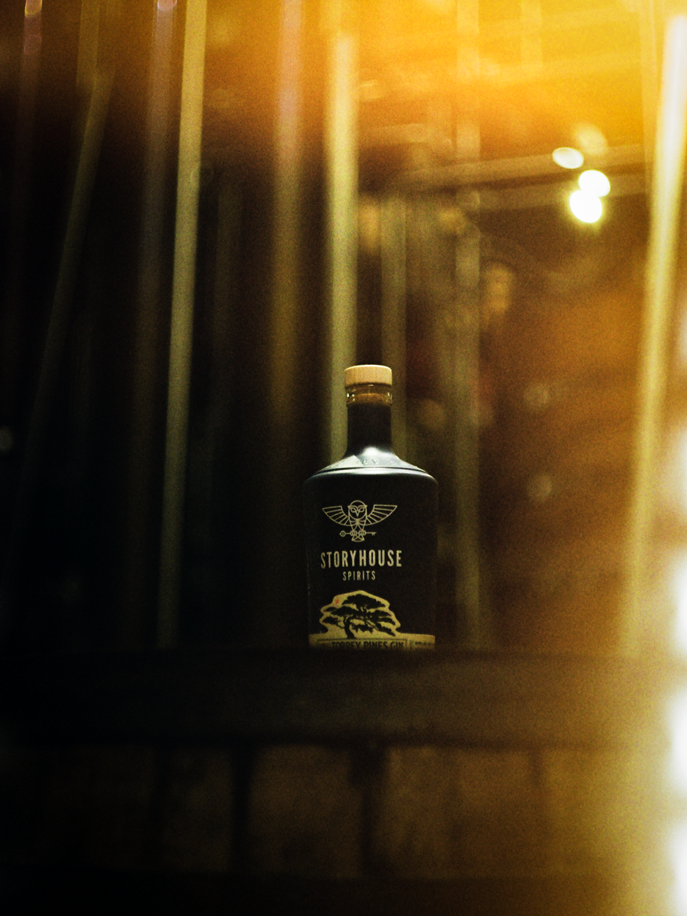 A Storyhouse Spirits bottle backlit by warm light through the doors in East Village, shot on 35mm film