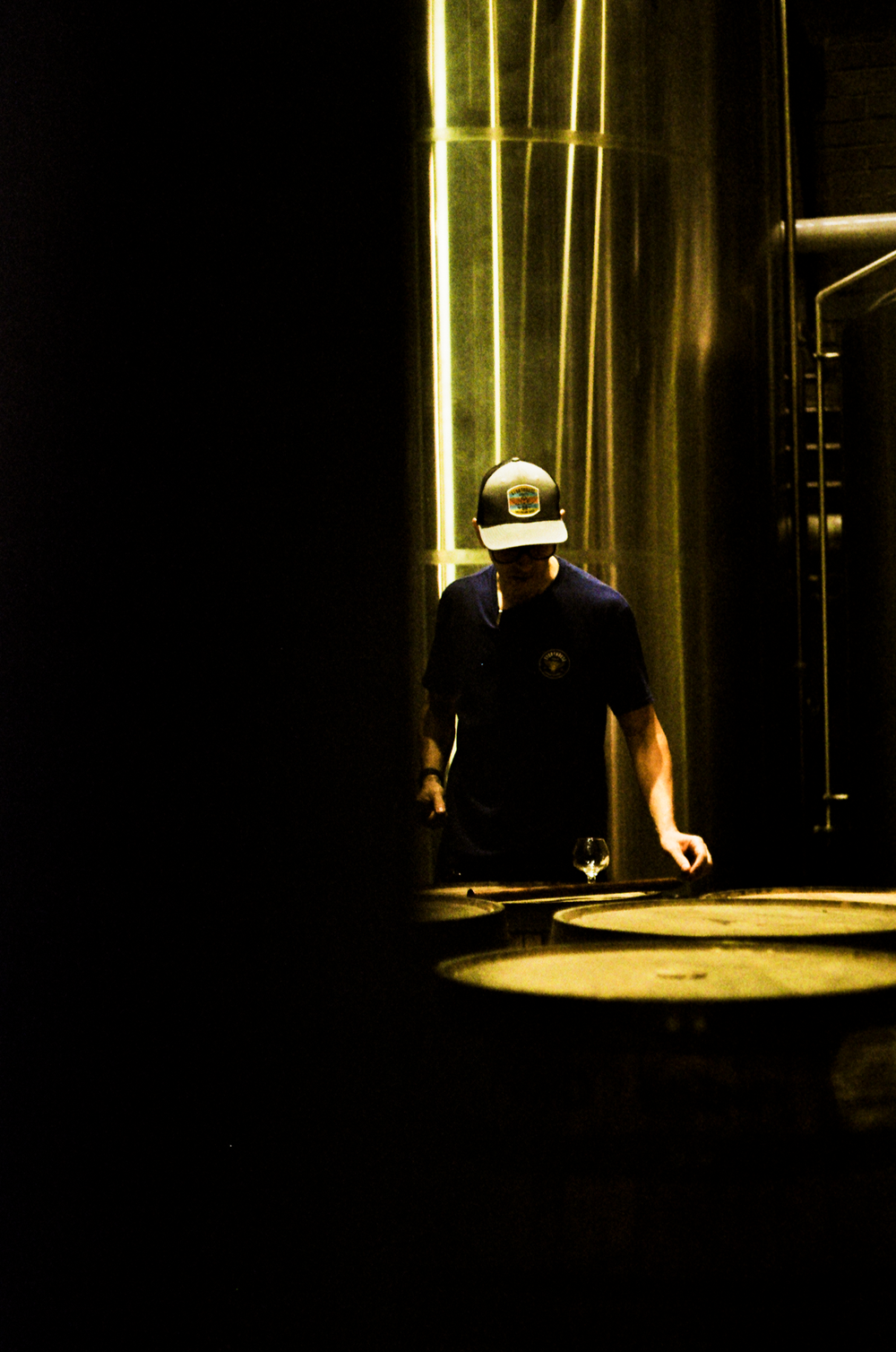 A distiller at a barrel in a shaft of light at Storyhouse Spirits in East Village, shot on 35mm film