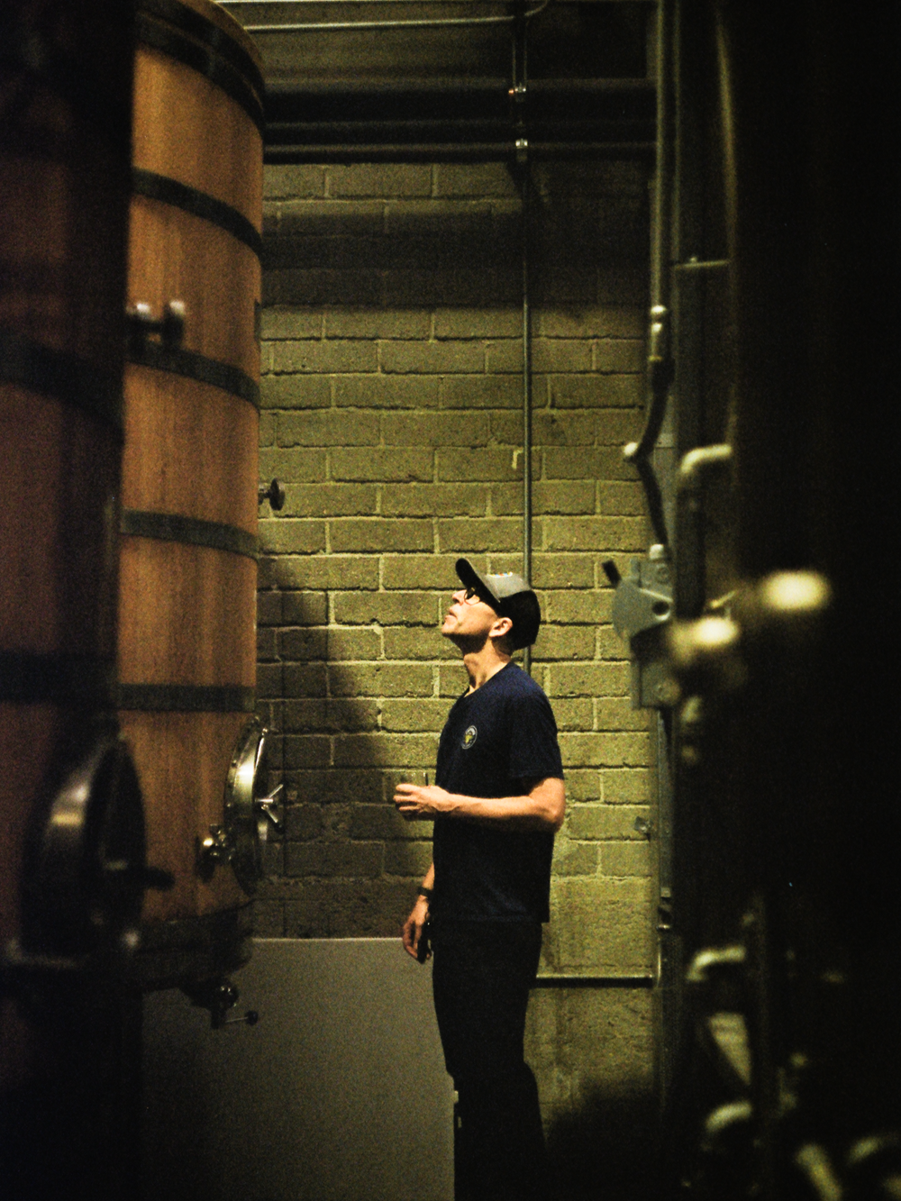 A distiller standing between barrels and the brick wall, shot on film
