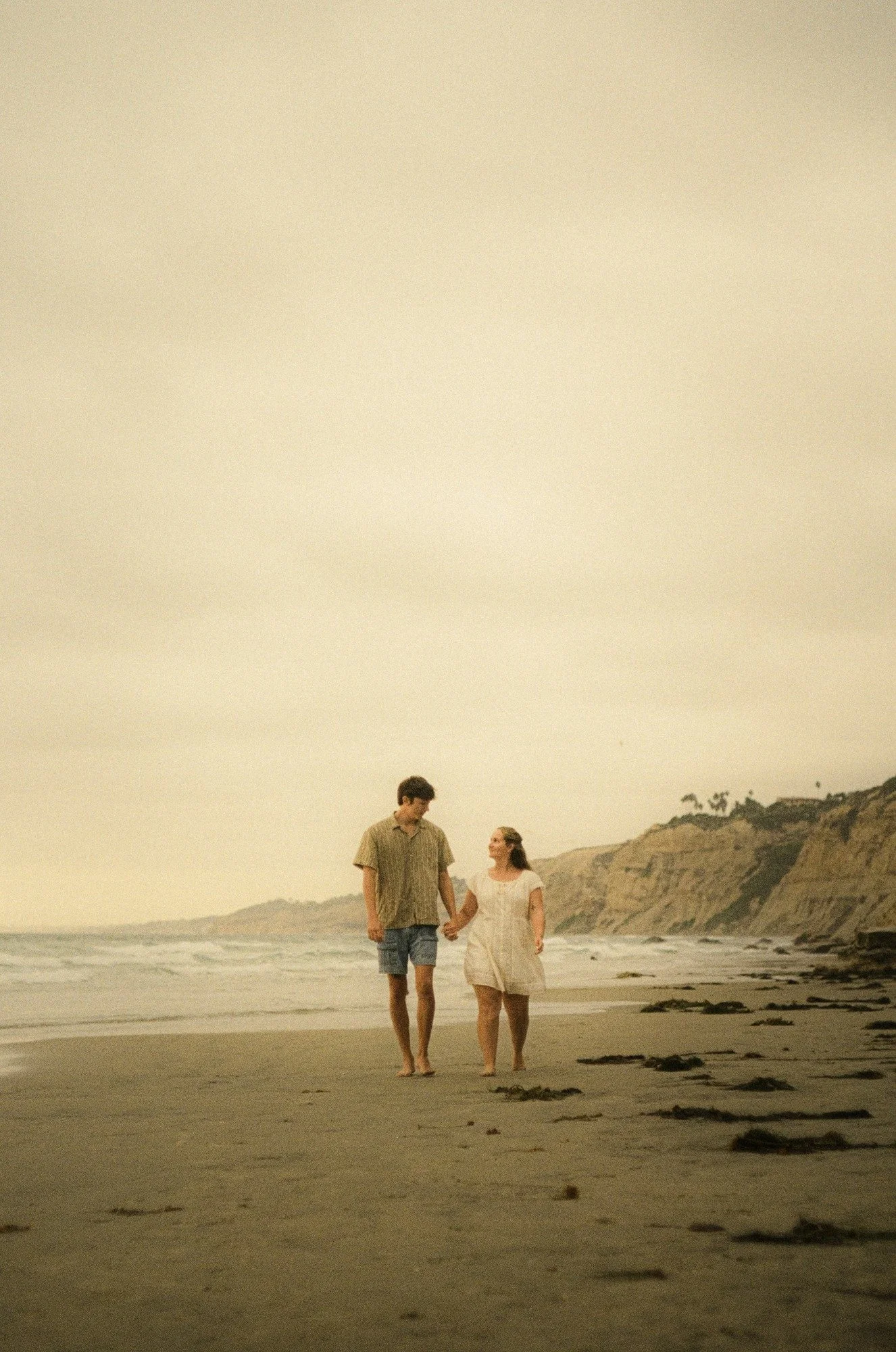 Rose and Brady walking along the beach toward the cliffs, shot on film