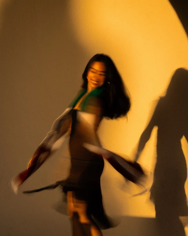 Magaly spinning in her graduation stole in front of a sunlit wall at SDSU