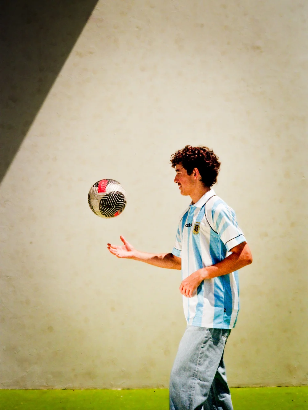 Juggling a ball in the Argentina kit in front of a sunlit wall
