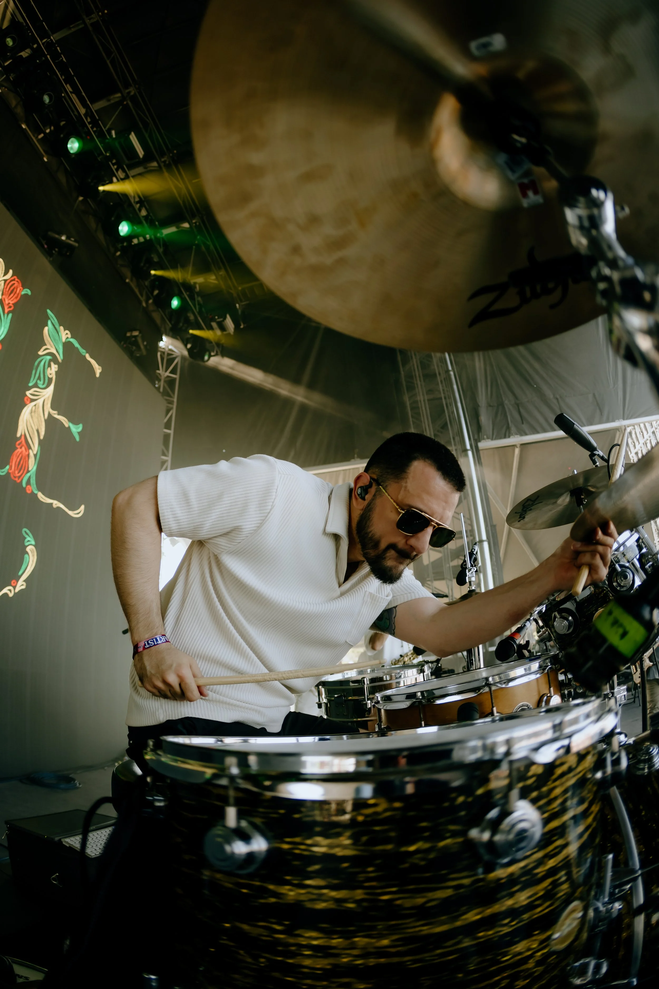 Musician playing drums on stage, with stage lighting and a digital screen in the background.