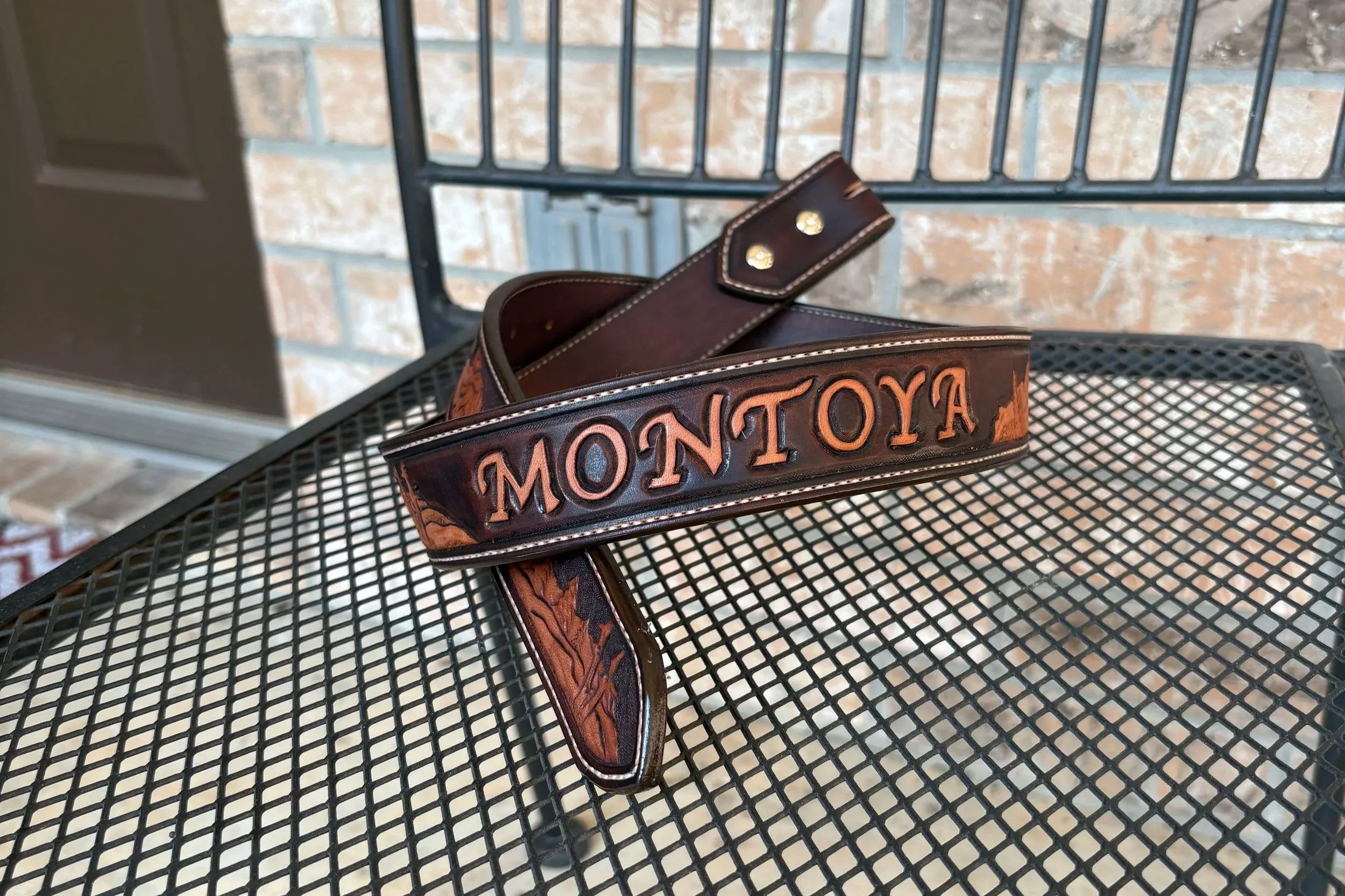A brown leather Toyota belt with embossed lettering, resting on a black metal mesh table against a background of brick wall and metal railing.
