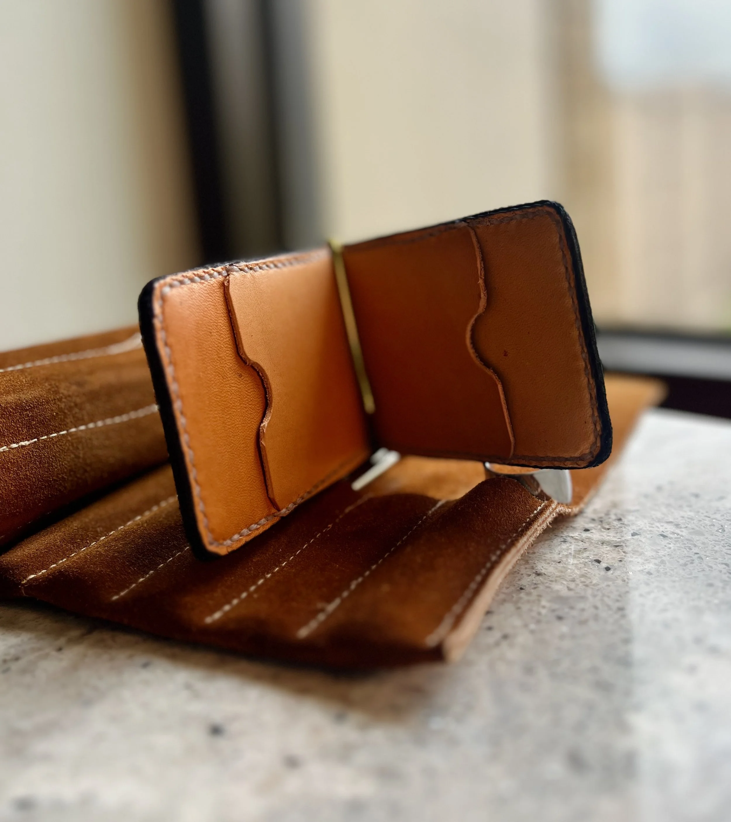 Close-up of a brown leather phone case with detailed stitching, resting on a light-colored textured surface.