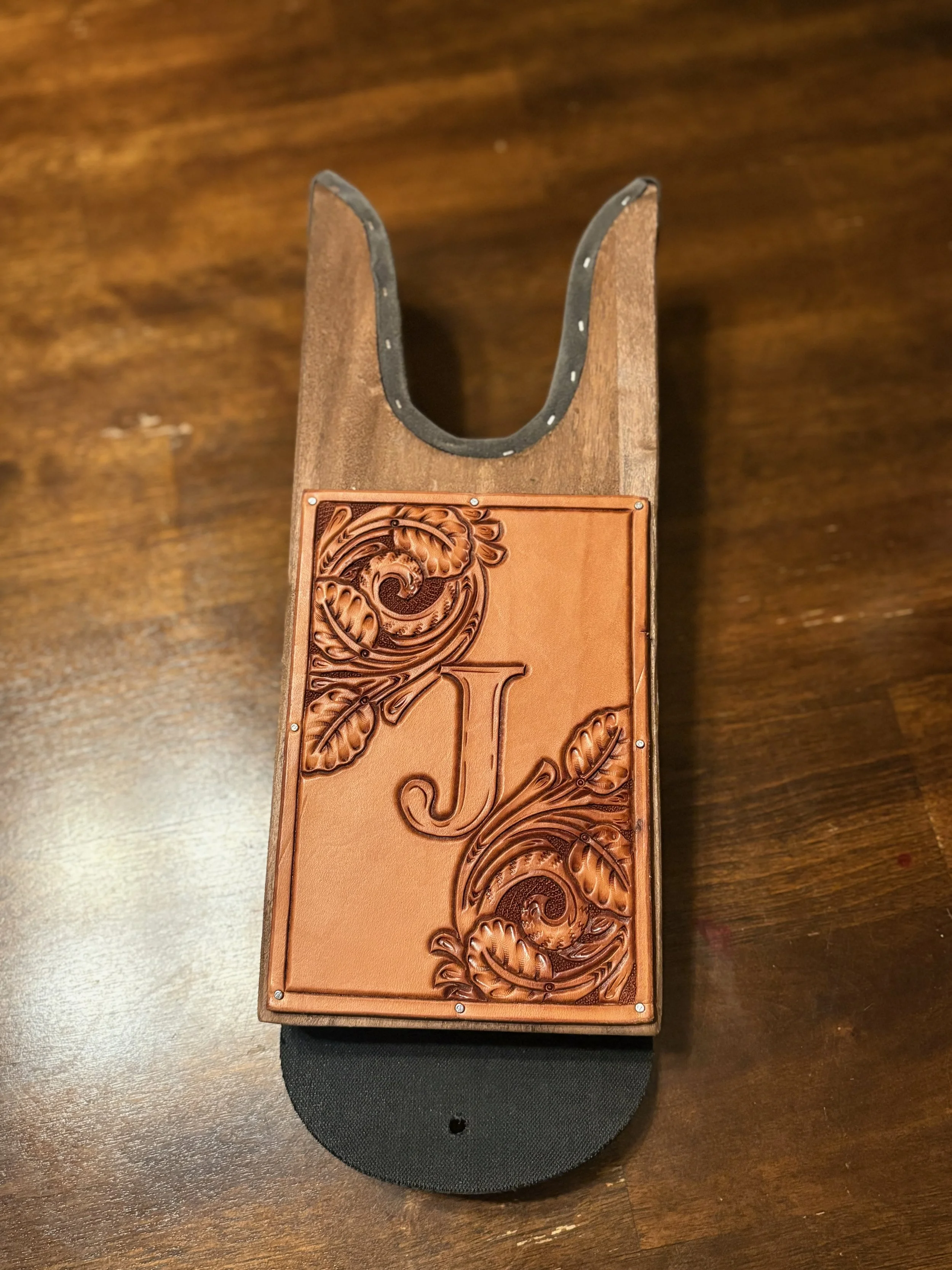 A wooden box with an ornate leather cover and a black base, placed on a wooden surface.
