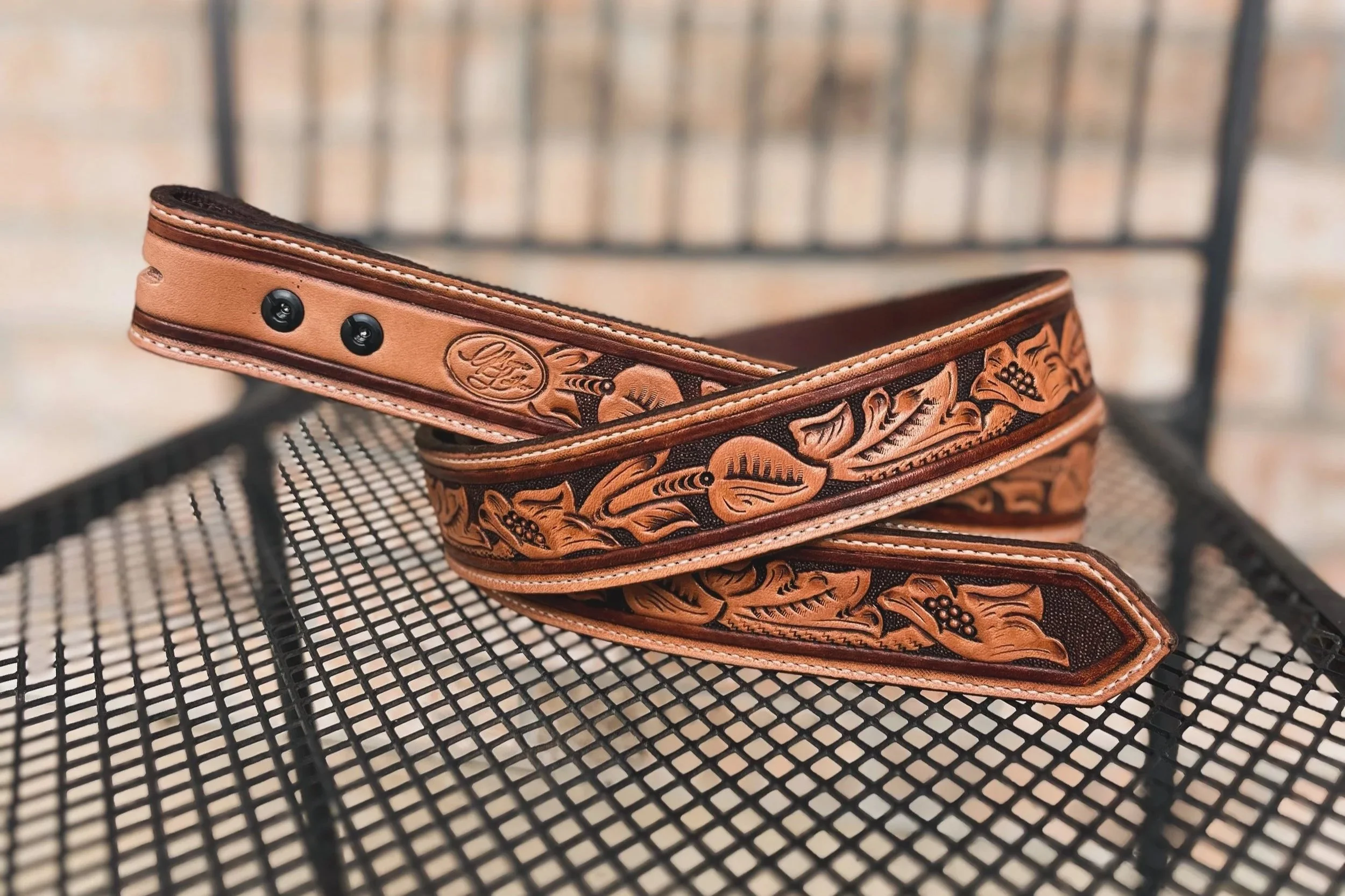 Close-up of a leather dog collar with engraved patterns, resting on a metal grid surface, with a blurred background.