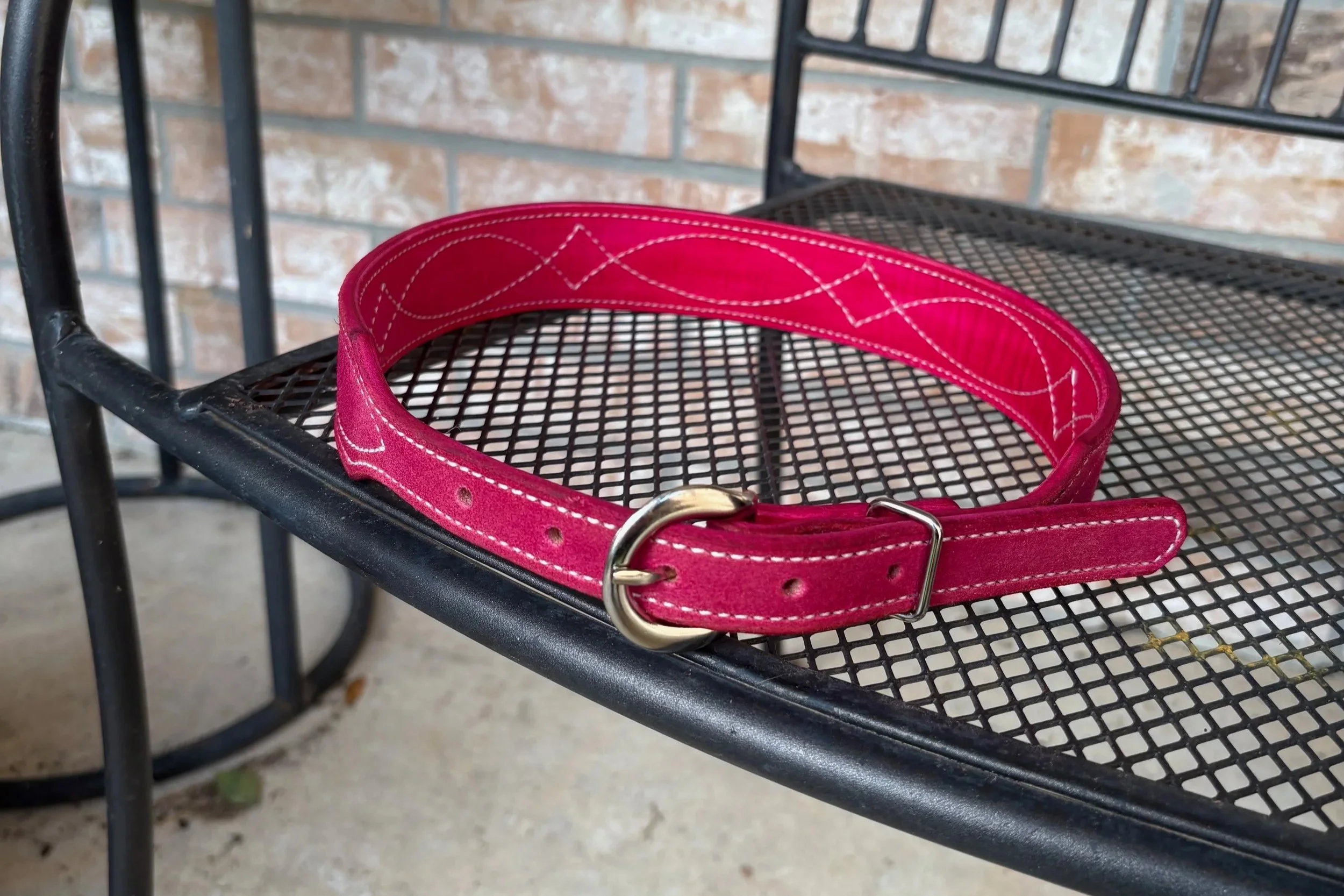 A red dog collar with white stitching resting on a black metal outdoor table with a brick wall background.