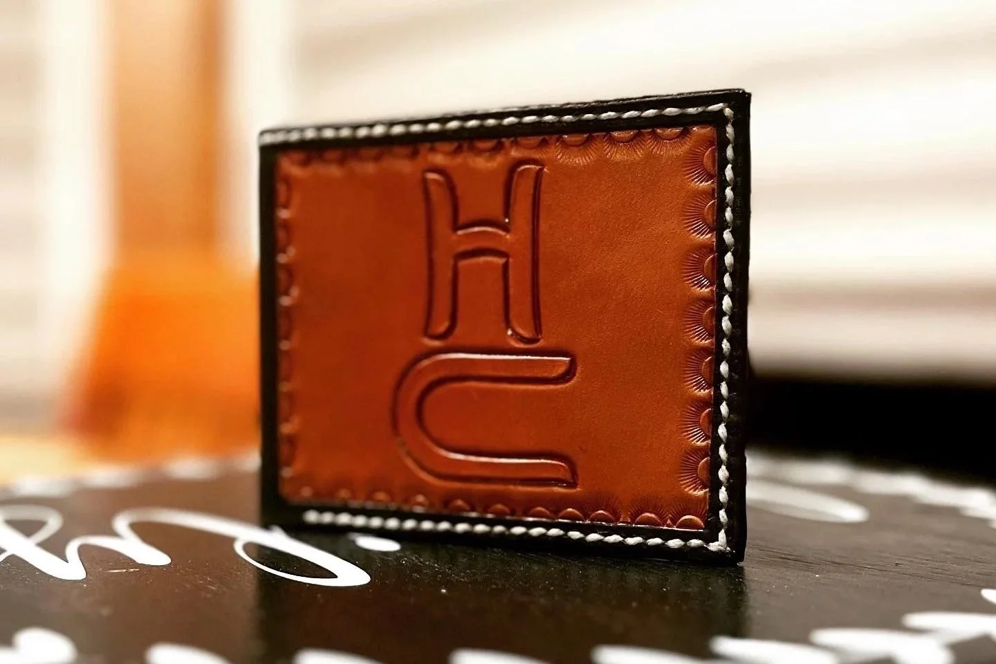 Close-up of a leather patch with embossed letter 'H' and 'C', stitched to a black surface.