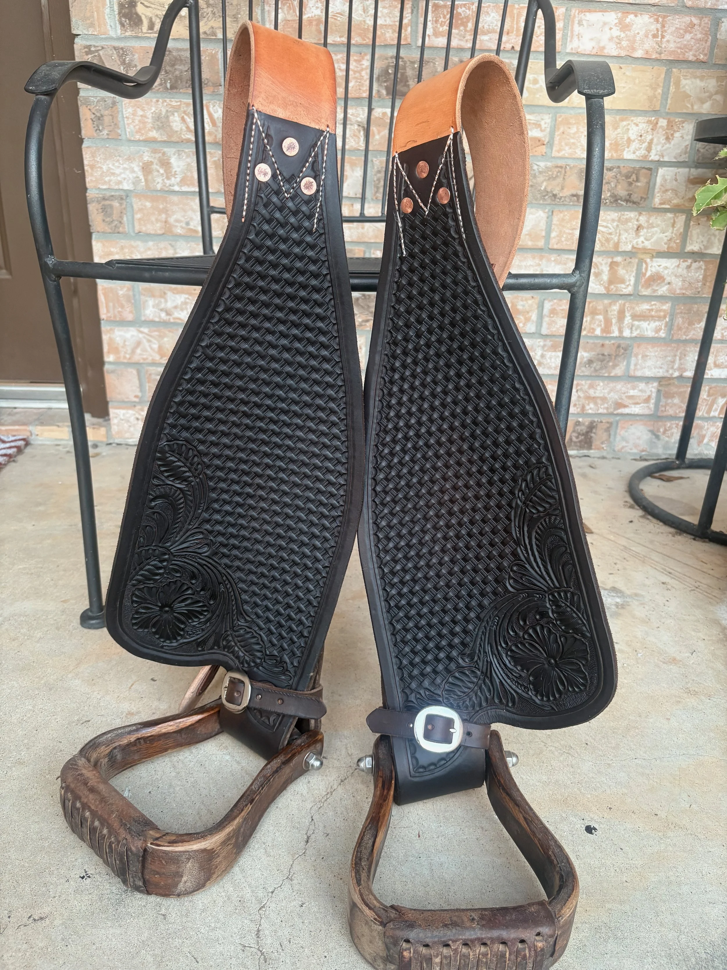 A pair of wooden sleds with black rubberized seats, positioned upside down on a concrete surface, with a brick wall background.