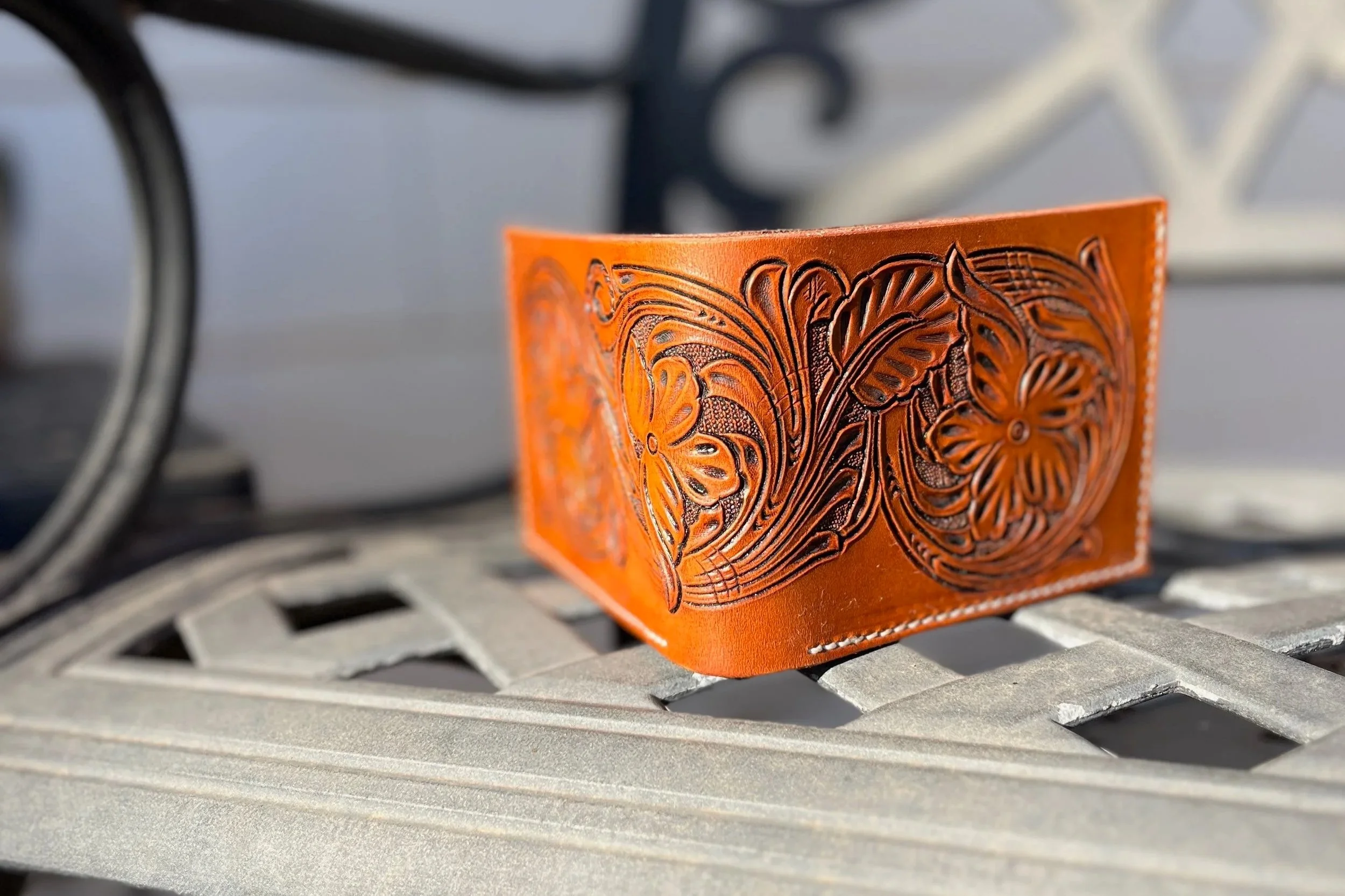 Close-up of an orange leather box with intricate butterfly and floral carved designs, placed on a metallic surface with a blurred background.