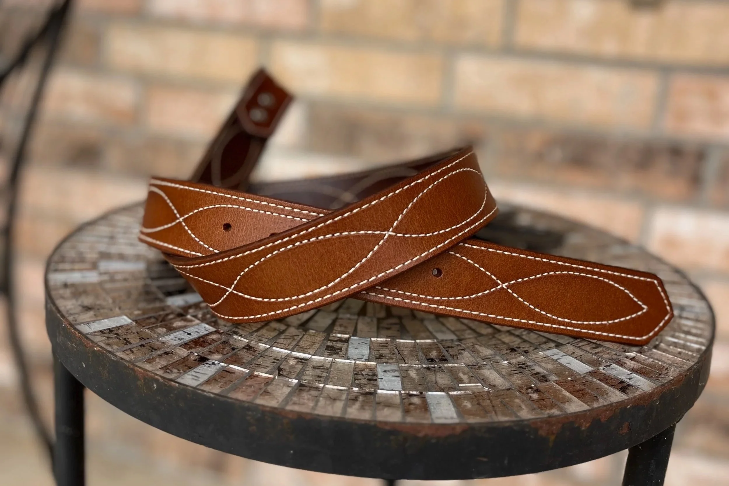 A brown leather belt with white stitching draped over a round, wooden, lattice-patterned table with a rustic appearance.