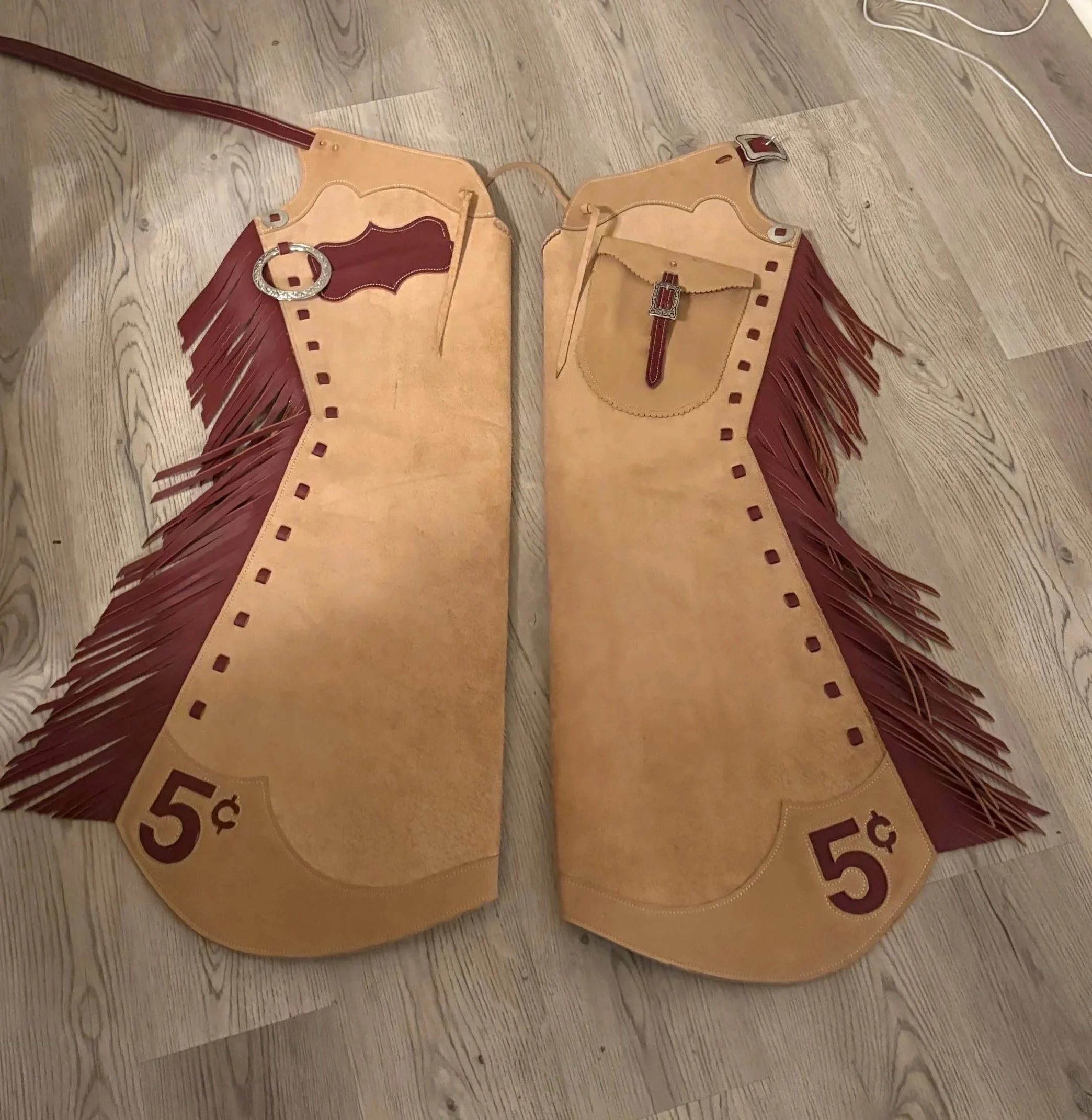 Leather fringed banner with a western style, featuring a pocket on each side, decorative buckles, and a price tag of 50 cents, laid out on a wooden floor.
