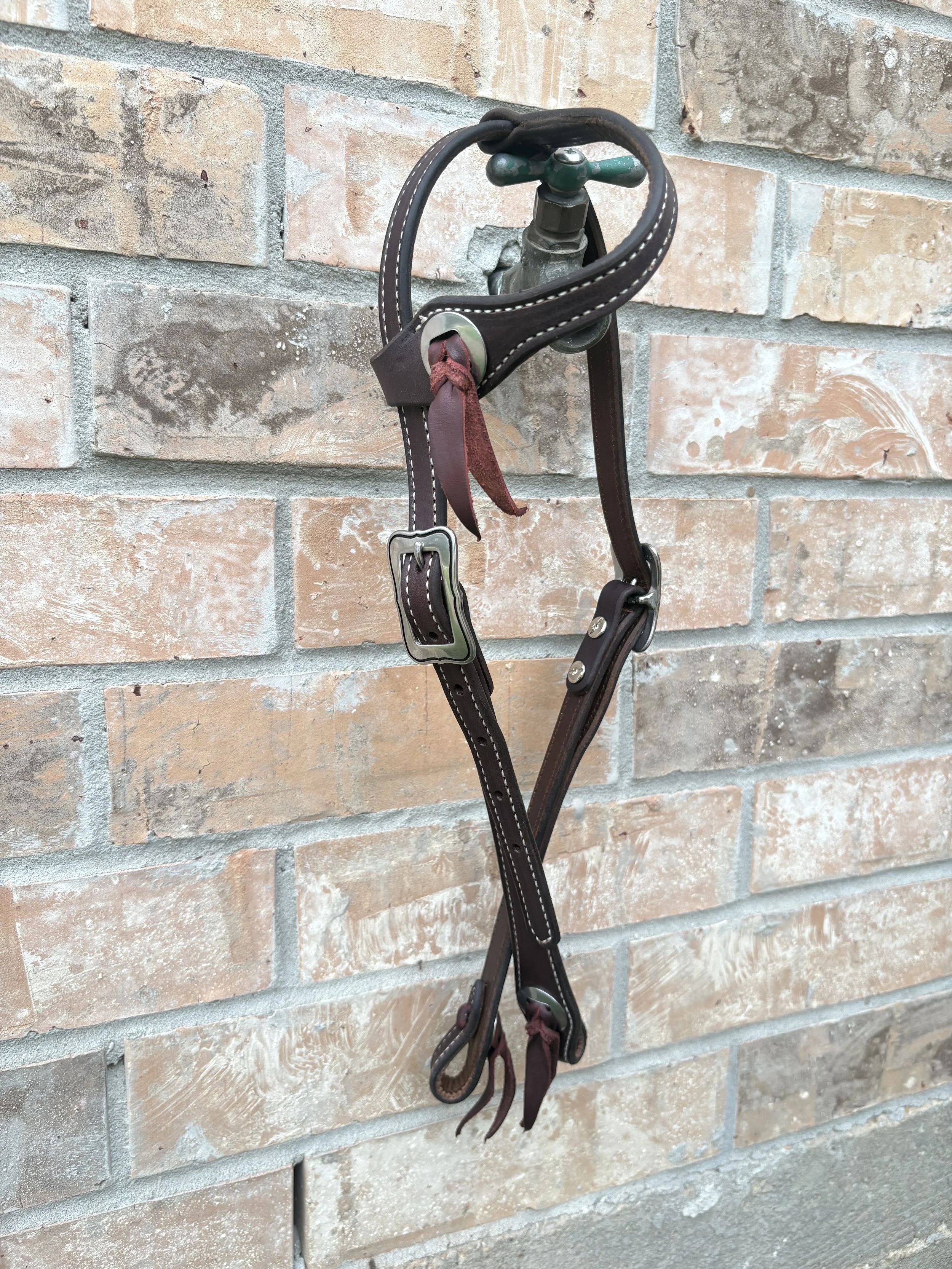 A collection of dark brown leather horse bridles hanging on a wall against a background of red and beige brick wall.