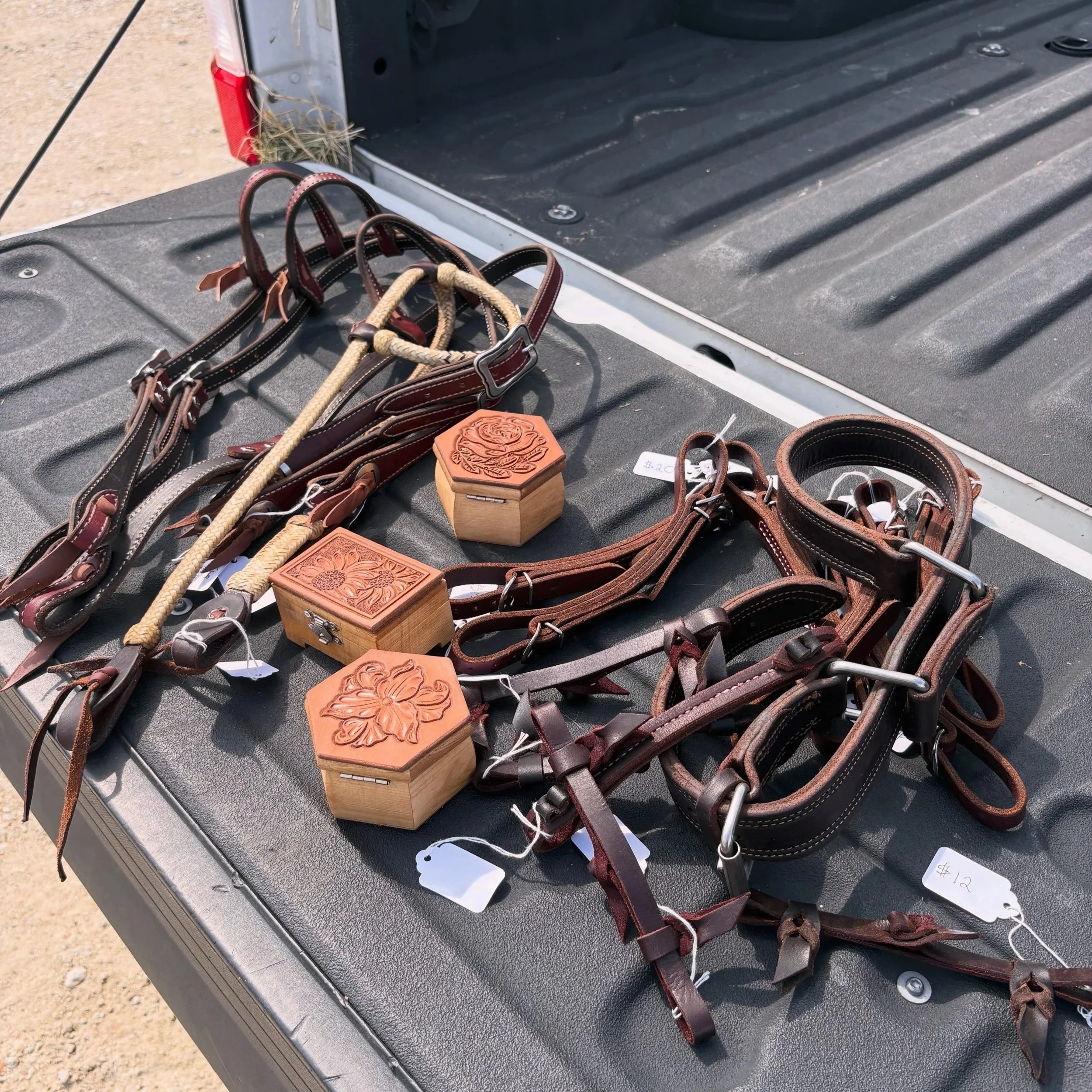 Various leather and rope horse reins and halters displayed on a black truck bed, with price tags attached.