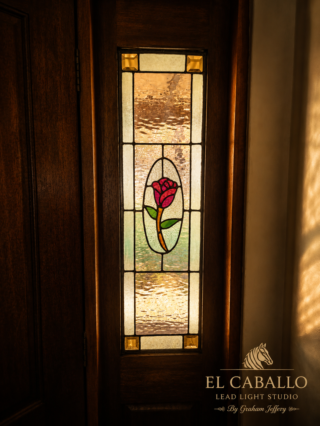 Decorative stained glass window with a pink rose in the center, surrounded by textured glass panes, wooden door frame, warm lighting.