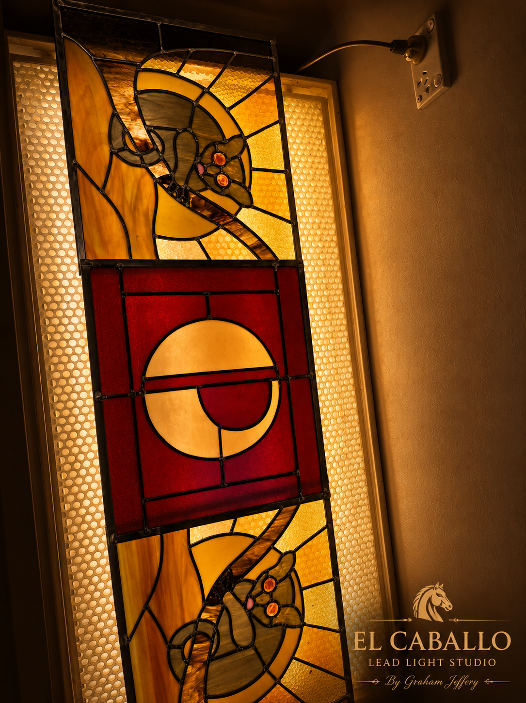 Stained glass window featuring a sun and moon design with warm yellow, orange, and red colors and intricate black outlining.