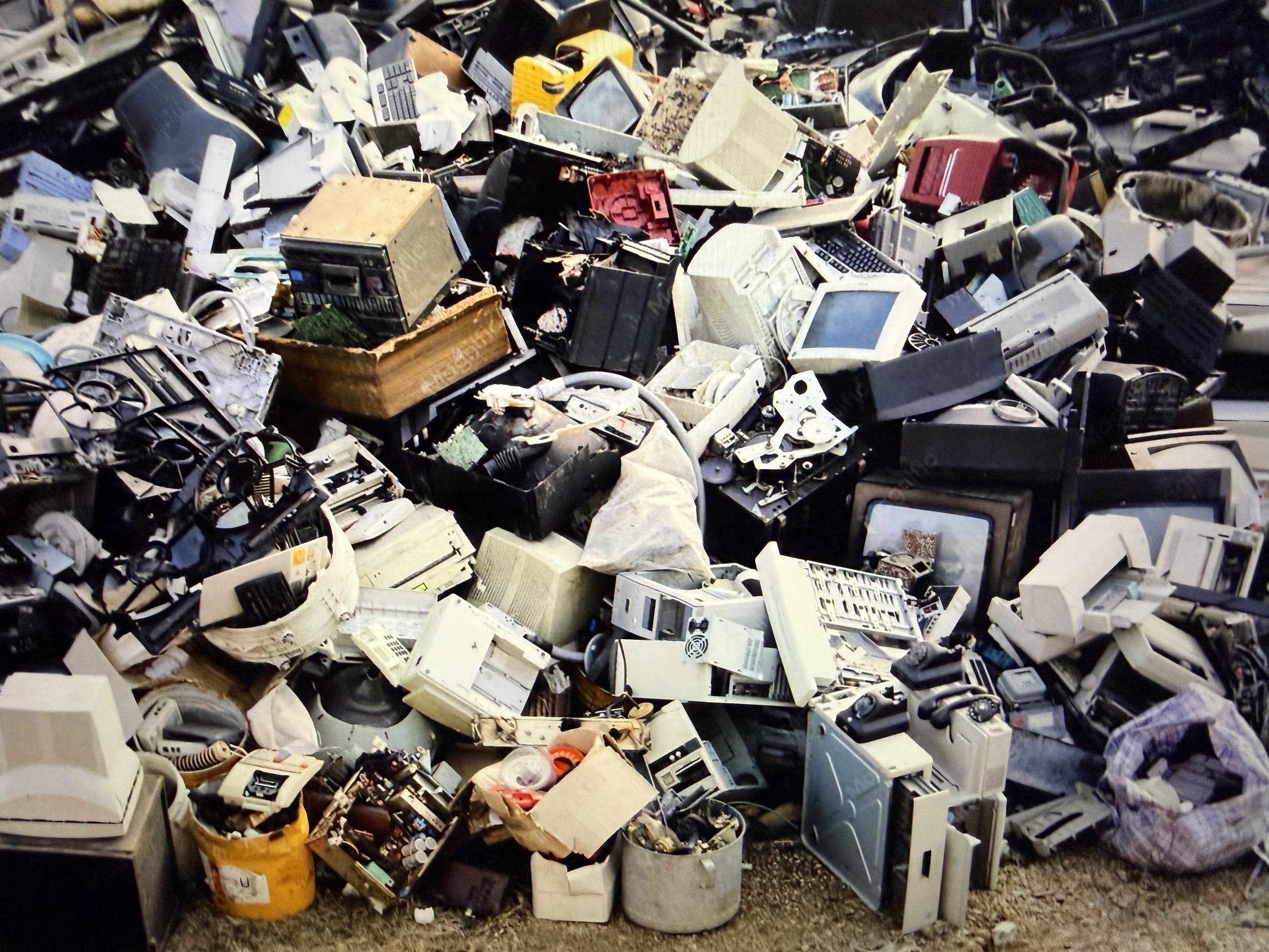 A large pile of discarded electronic waste, including old computers, monitors, keyboards, and various electronic components.