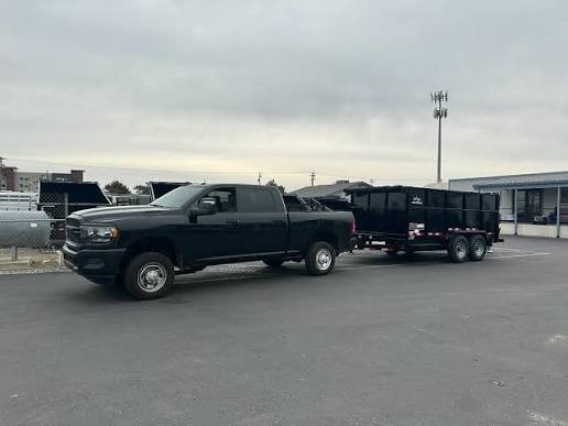 Black pickup truck towing a black trailer in a parking lot on a cloudy day.