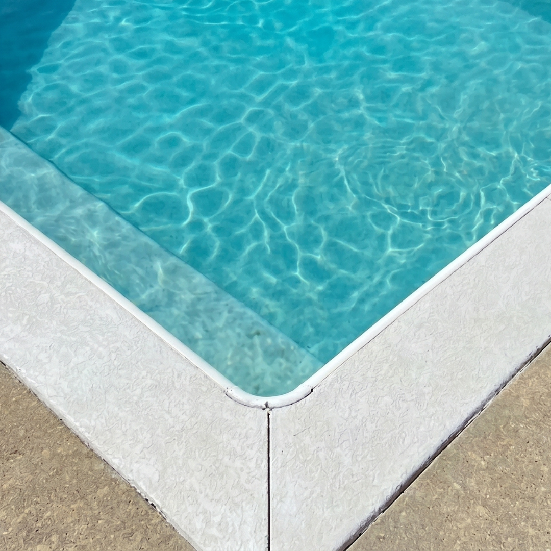 Close-up of a swimming pool corner with clear blue water and white textured pool edge.