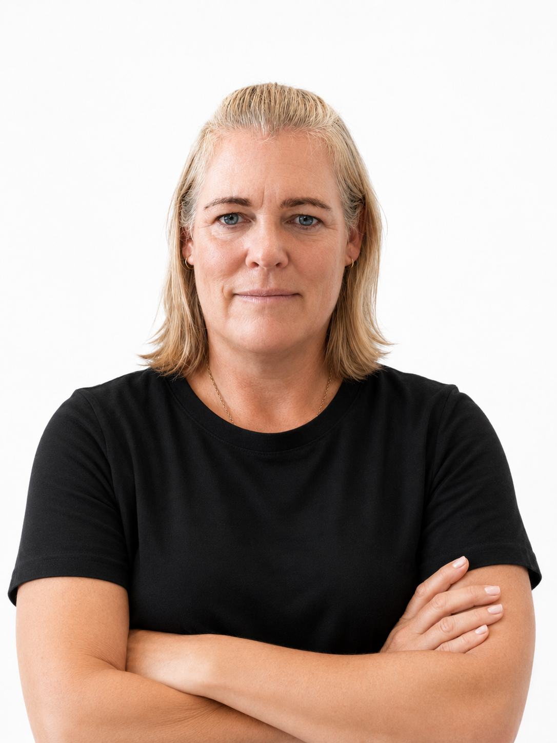 Portrait of a middle-aged woman with blonde hair, blue eyes, wearing a black t-shirt, arms crossed, against a plain white background.