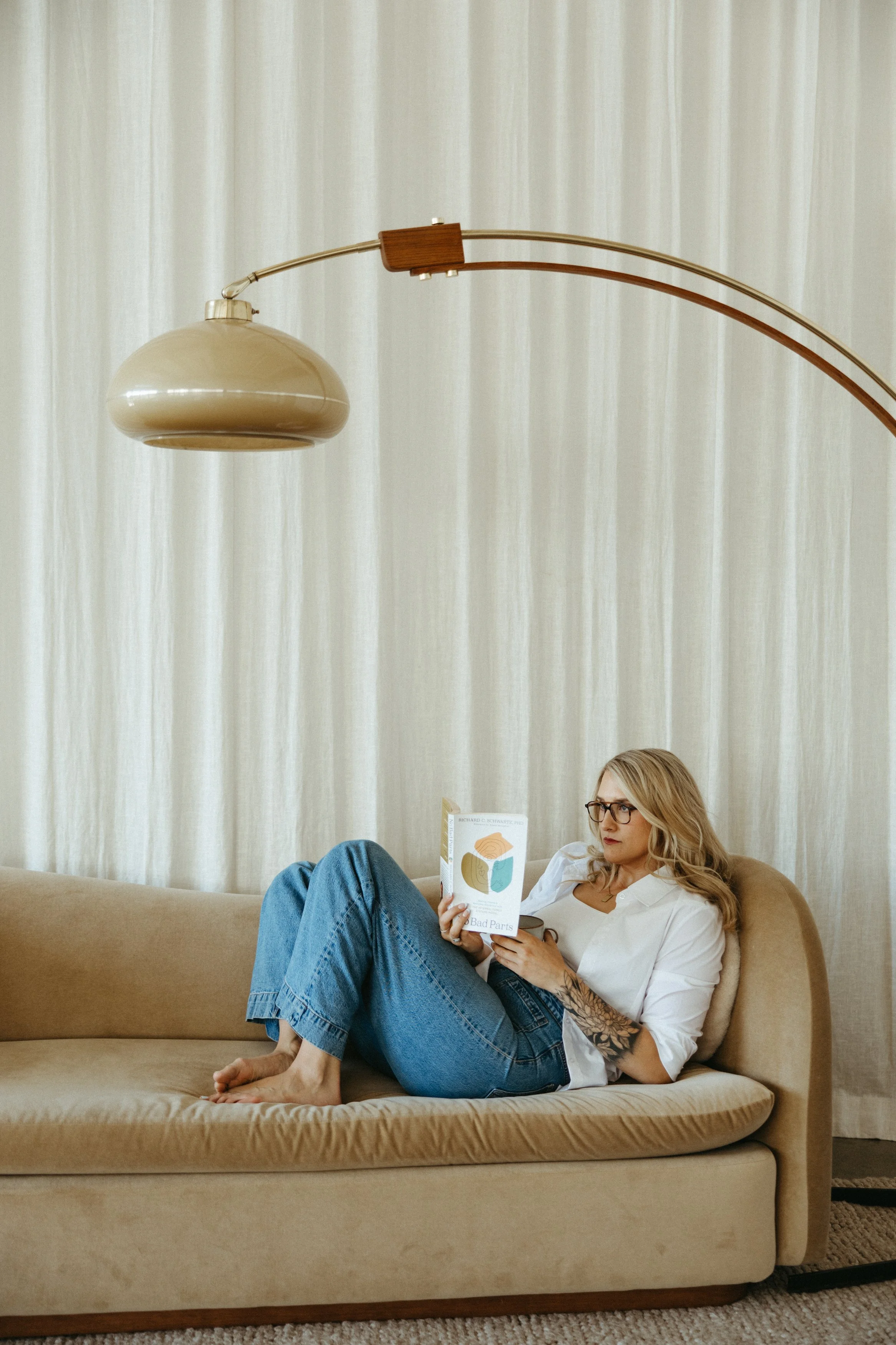 Hannah Guy, LCSW, trauma therapist, sitting in a chair reading a book about Internal Family Systems (IFS) therapy.