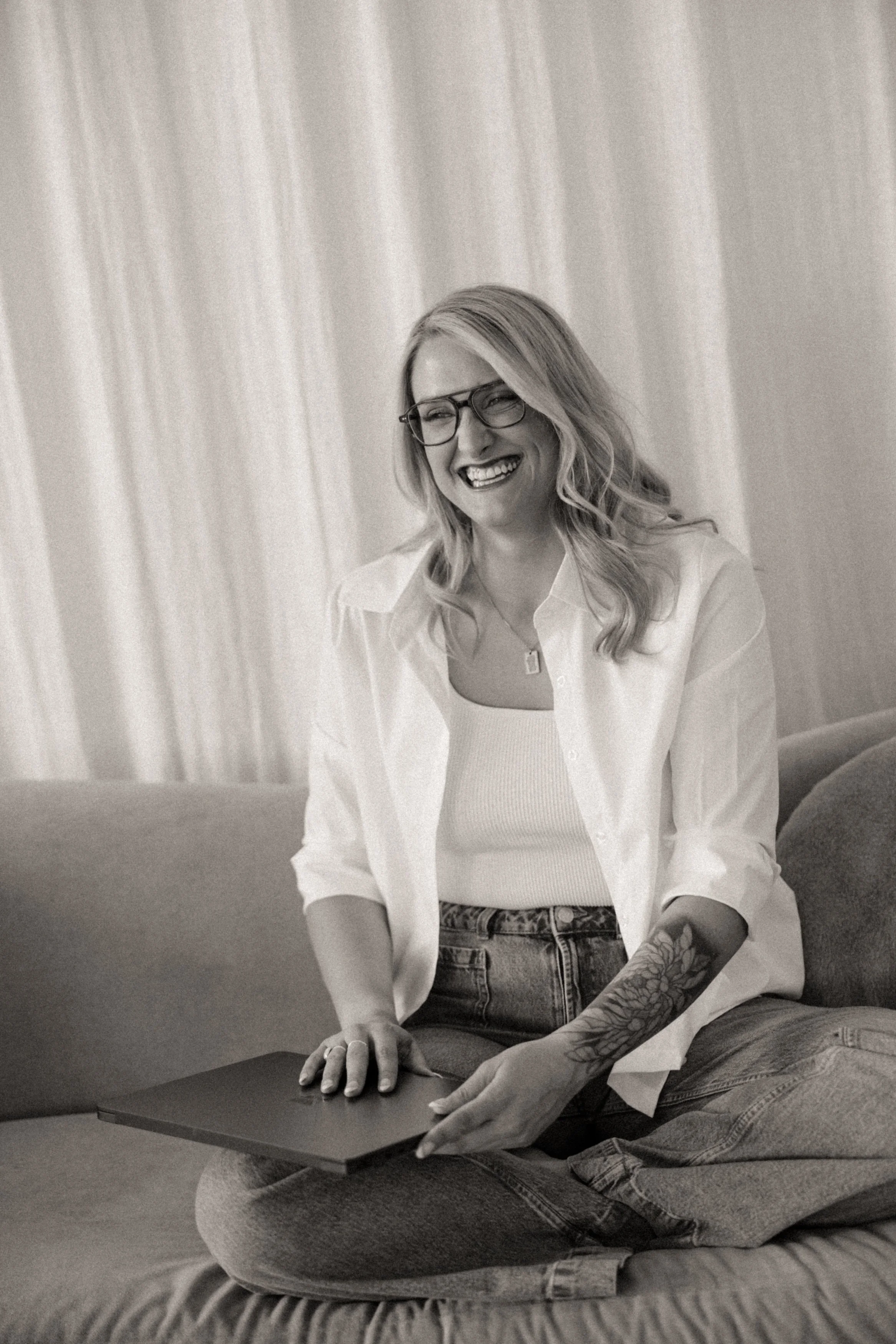 Smiling online EMDR and trauma therapist opening up computer while sitting on couch.