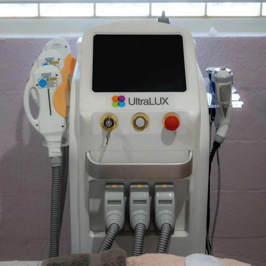 Medical laser machine labeled UltraLUX with various controls, hoses, and attachments in a clinical setting.