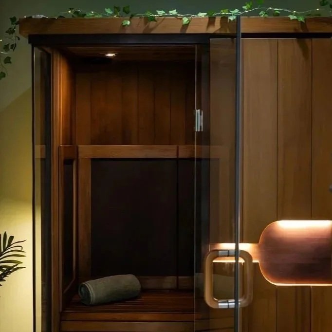 Glass door sauna with wooden interior, towel inside, and a small plant to the side.