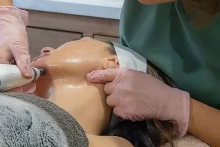 A person receiving a facial treatment with a facial device while lying down, with a skincare professional applying the treatment.