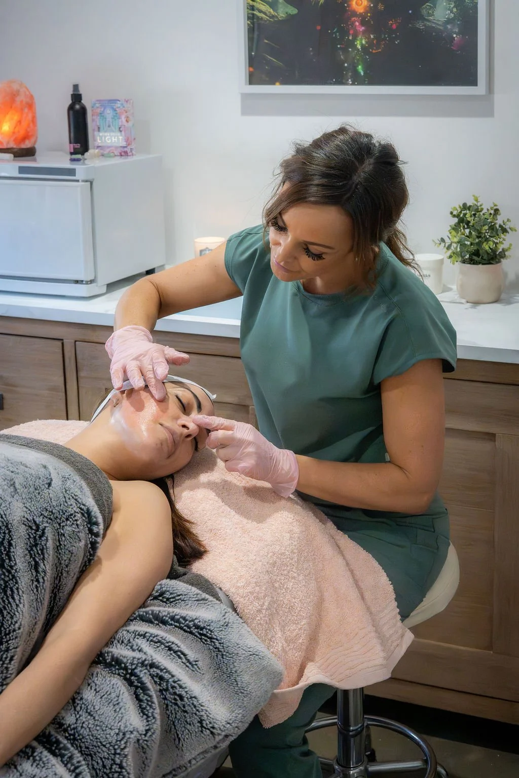 A woman receiving a facial treatment from a skincare professional in a spa or skincare clinic.