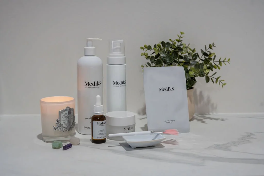Skincare products, a lit candle, a potted plant, and a tray with small items on a marble surface.