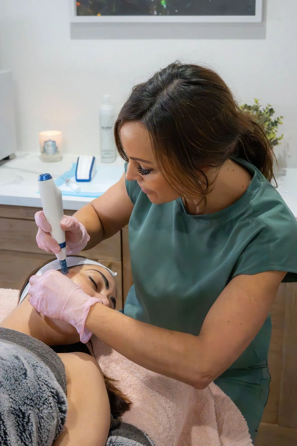 A woman receiving a facial treatment from an esthetician in a spa or clinic setting.