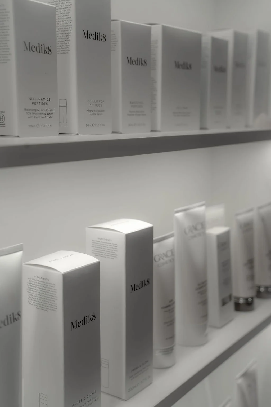 Rows of white Medik8 skincare products, including serums and creams, displayed on shelves in a minimalist setting.