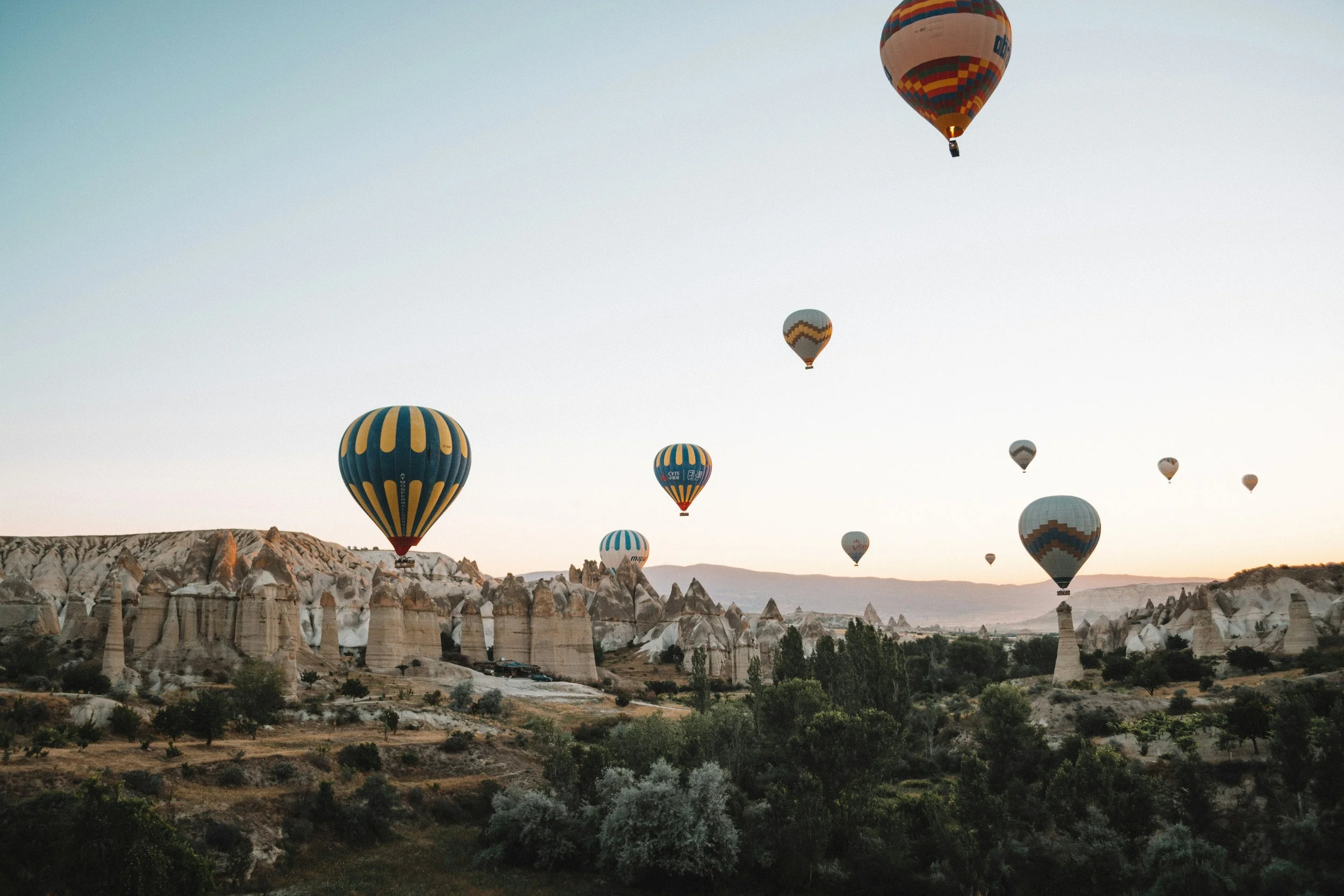 Multiple colorful hot air balloons floating over a rocky landscape at sunset.