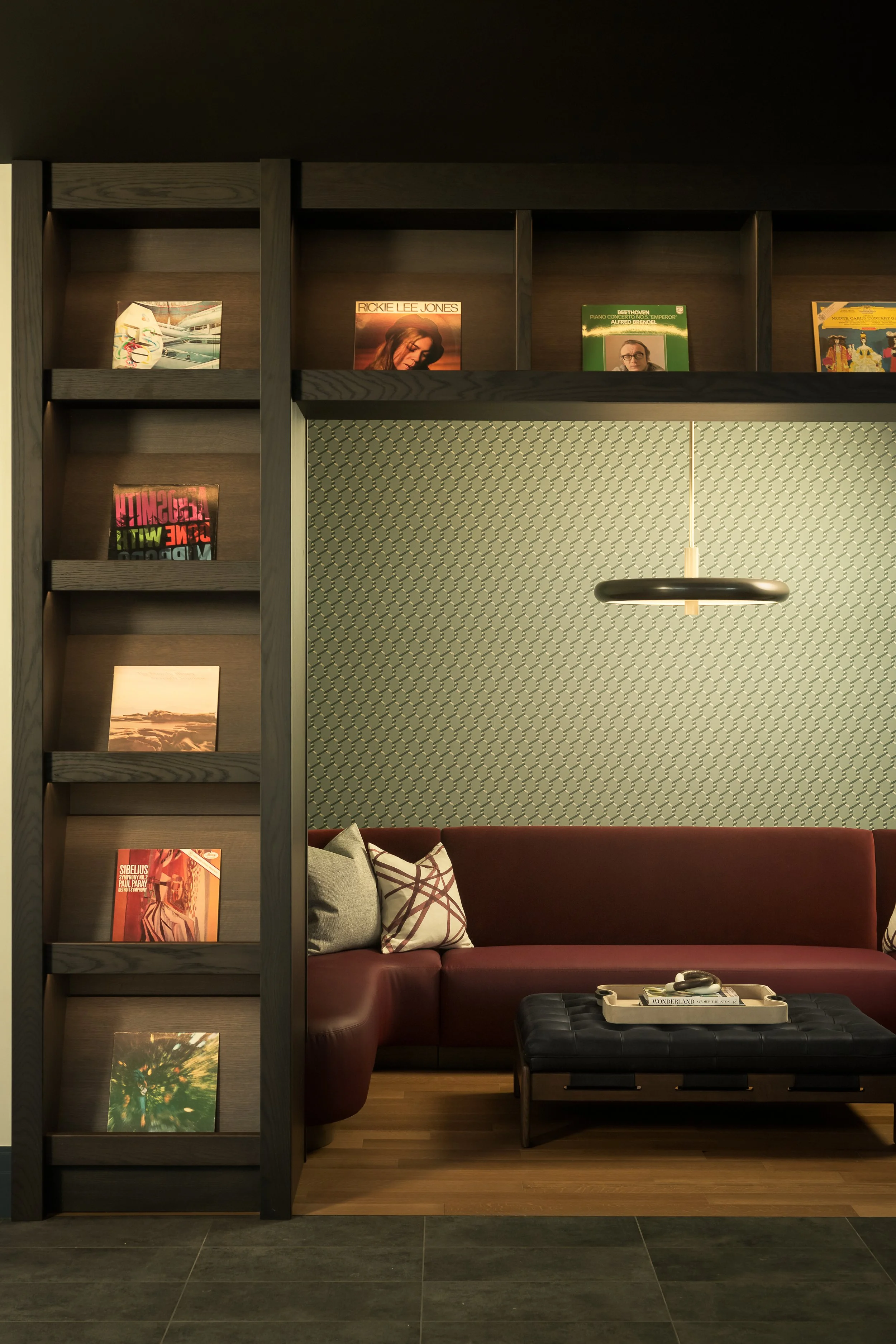 Intimate lounge nook with custom built-in shelving, textured accent wall, and rich burgundy banquette — interior design photography, Milwaukee WI