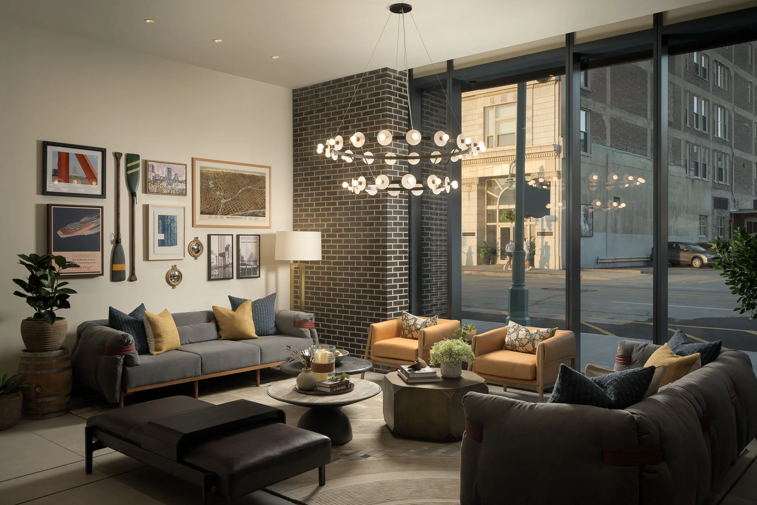 Elegant resident lounge with sputnik chandelier, grey and tan sofas, and city-facing windows — luxury interior photography, 333 Water Milwaukee WI