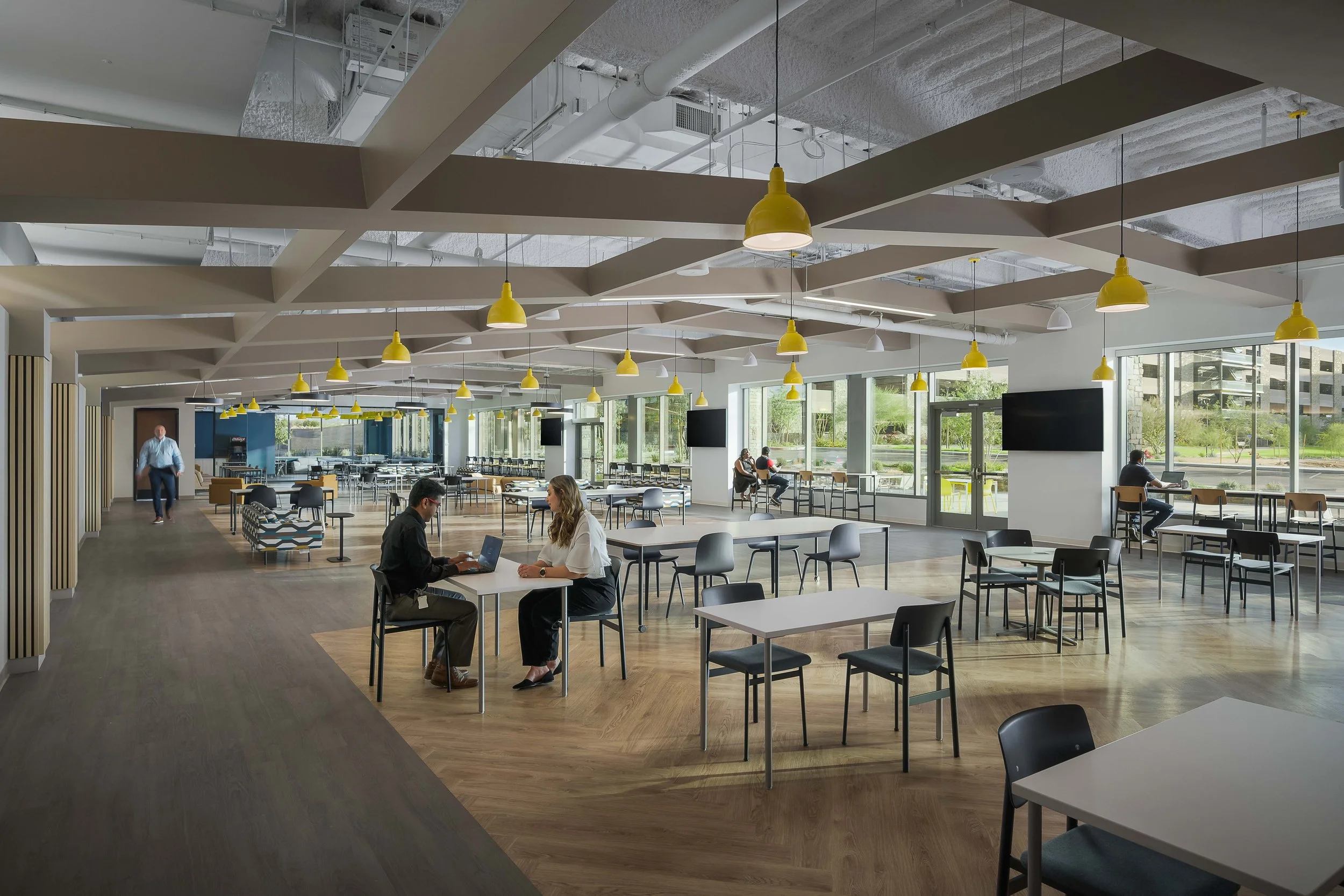 Bright open-plan collaborative office with yellow pendant fixtures, work tables, and digital display wall — corporate interior photography, Choice Hotels Scottsdale AZ