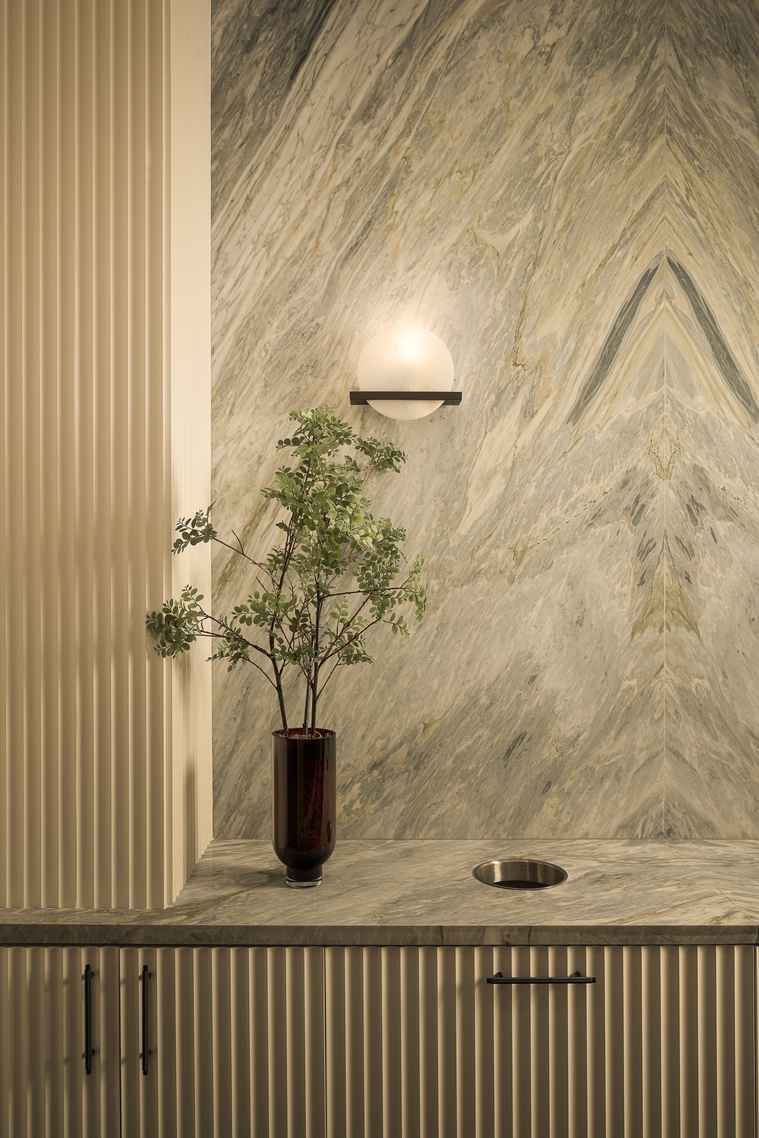 Luxury marble entry with fluted column, modern wall sconce, and sculptural statement plant — high-end residential interior photography, Fort Lauderdale FL