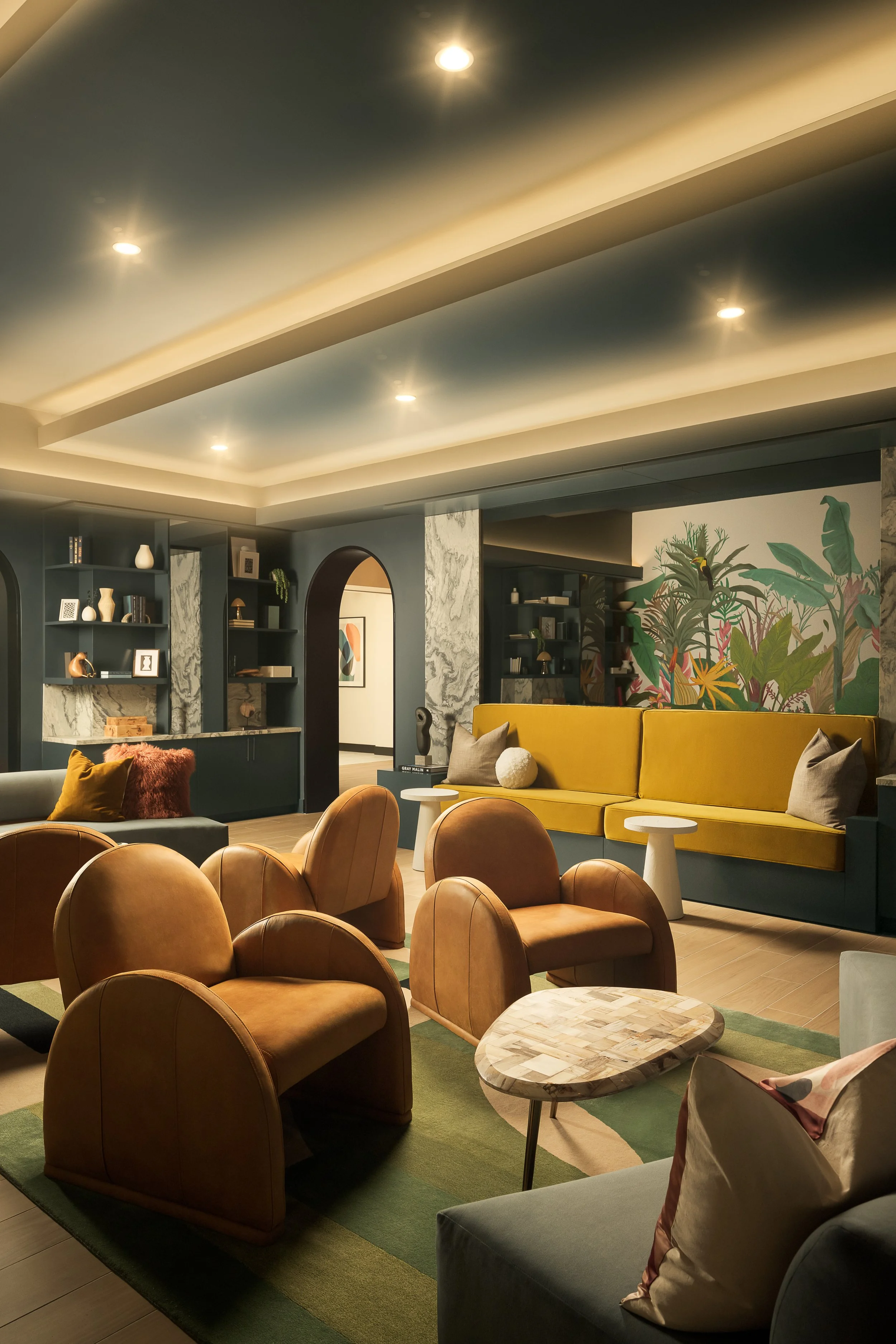 Moody lounge with arched doorways, mustard yellow sofa, tan barrel chairs, and tropical plants — luxury apartment interior design, Coasterra Fort Lauderdale FL