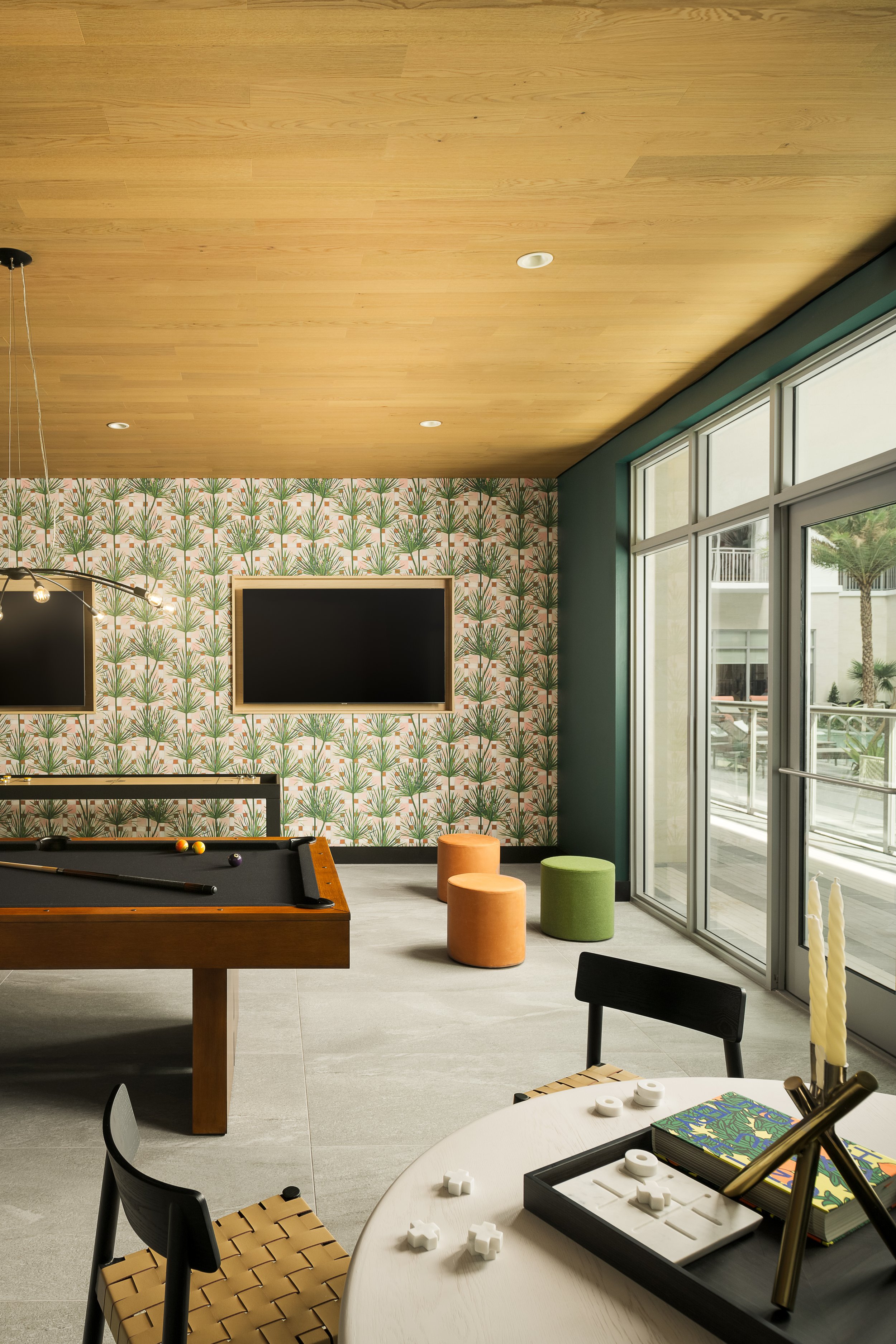 Resident game room with botanical wallpaper, billiards table, and warm wood ceiling — boutique apartment amenity design, Fort Lauderdale FL