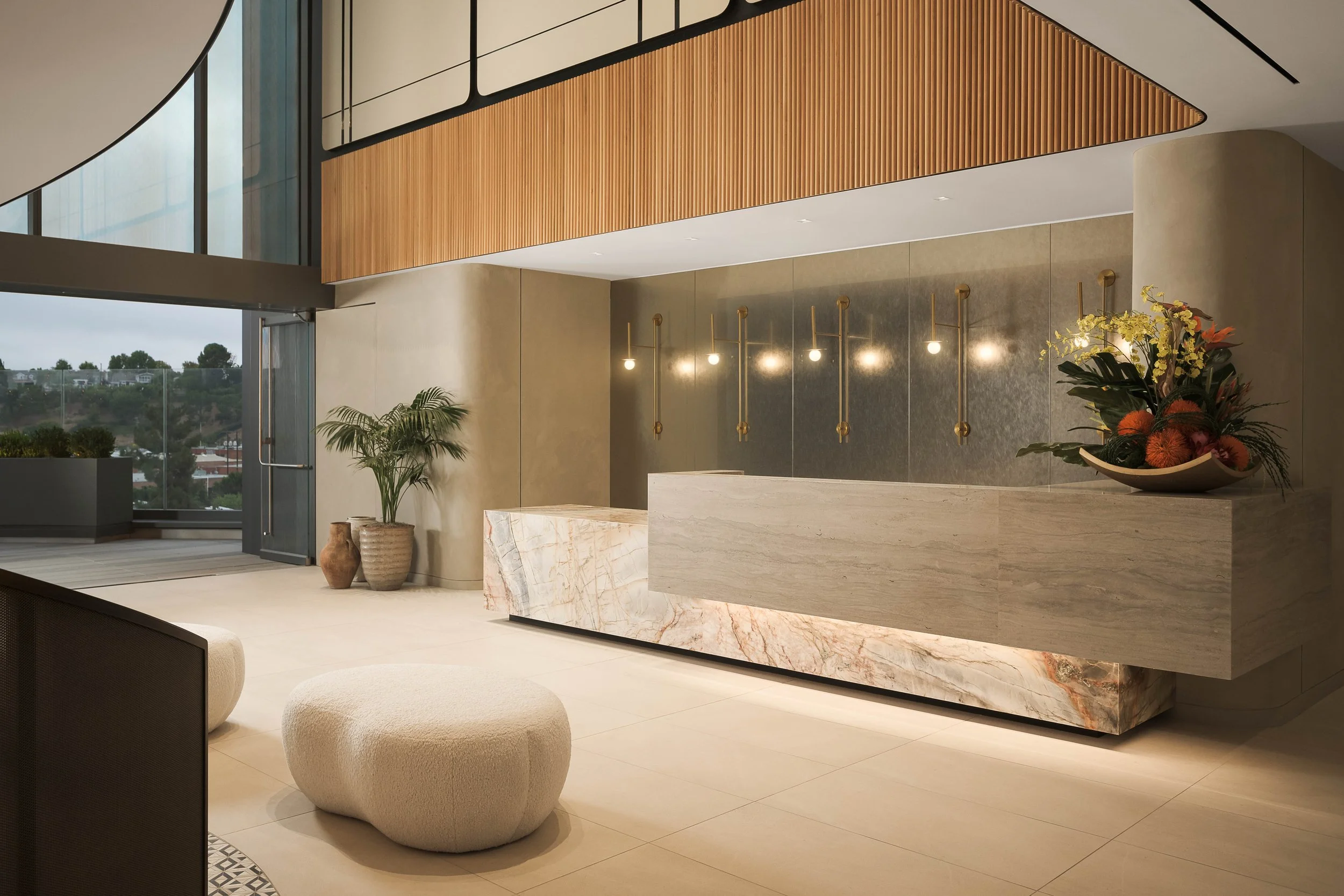Open lobby atrium with wood slat ceiling accents, marble reception counter, and sculptural seating — commercial architecture photography, Los Angeles CA